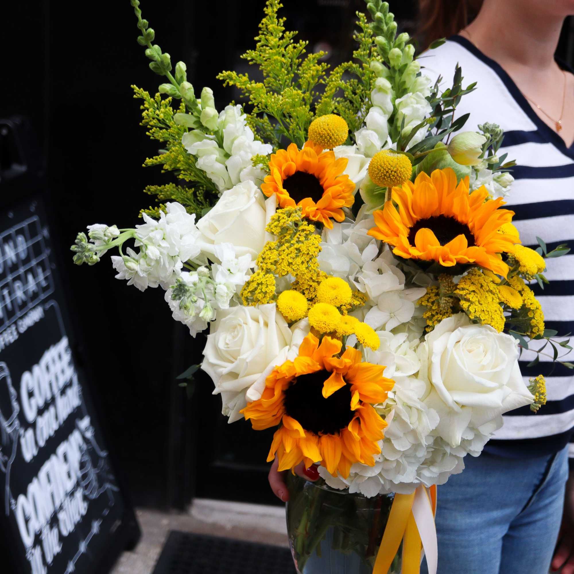 Bouquet of sunflowers, white roses, and white hydrangeas in a glass vase