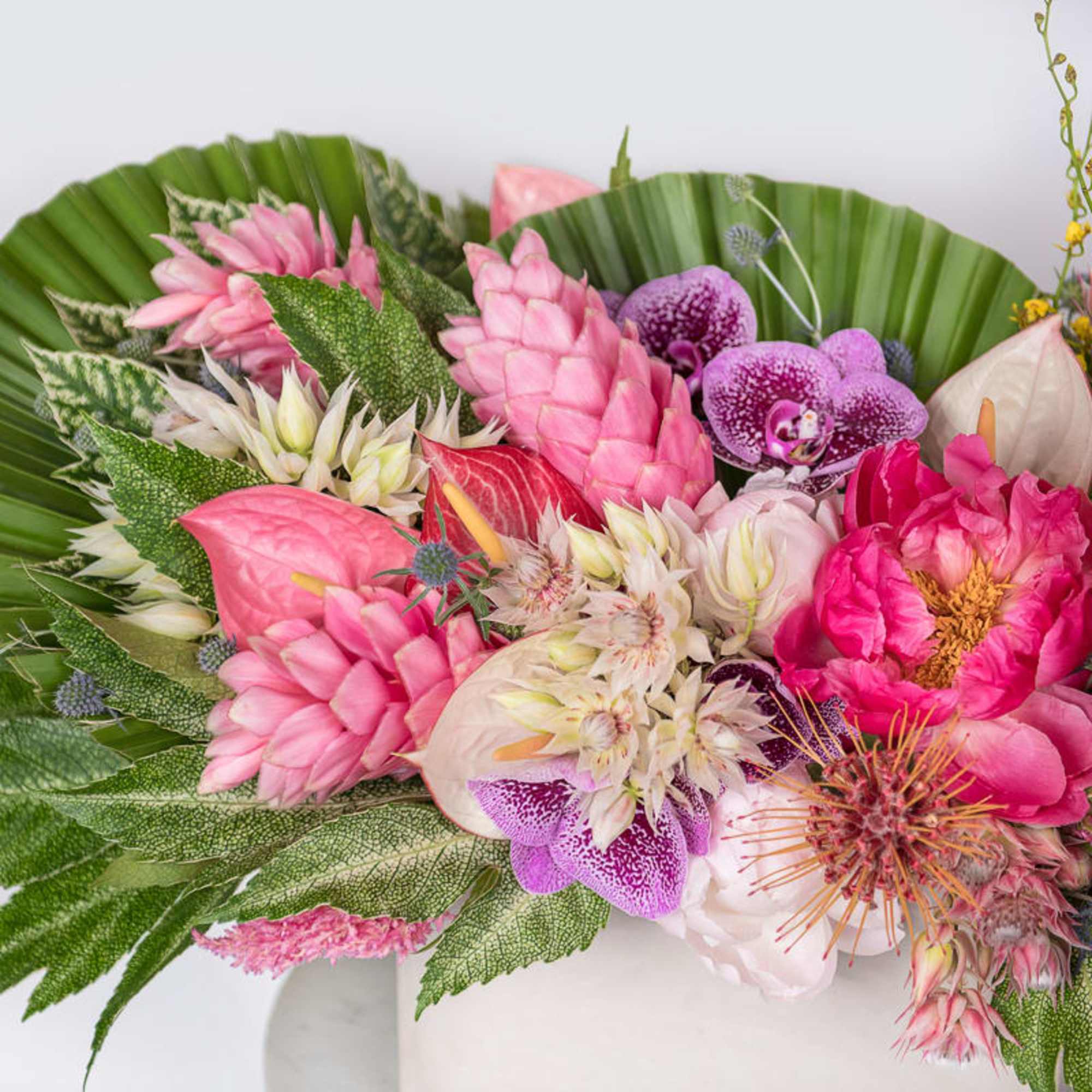 Vibrant pink tropical flower arrangement with orchids and peonies in a white vase