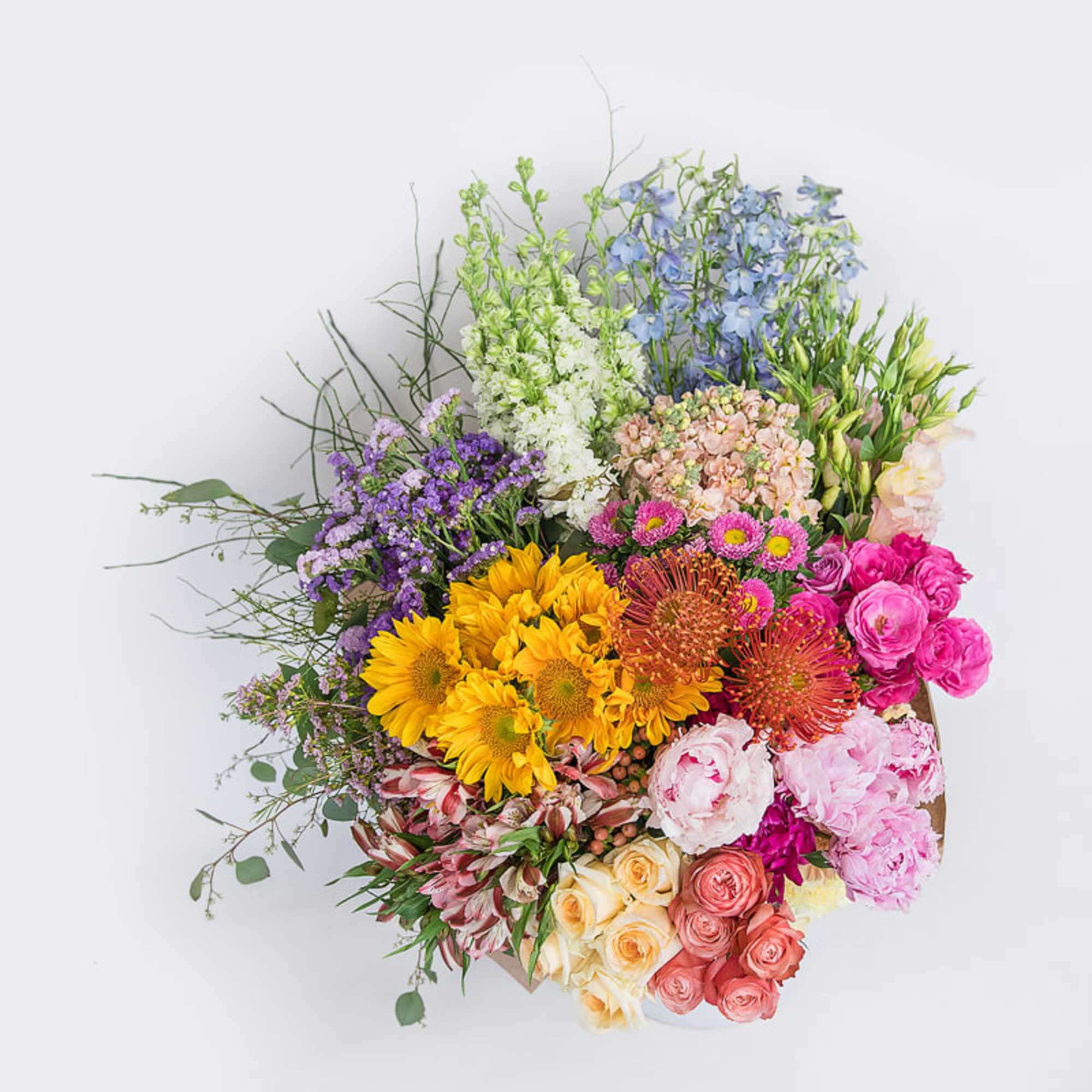 Colorful mixed flower arrangement with sunflowers, roses, protea, and peonies in a low container