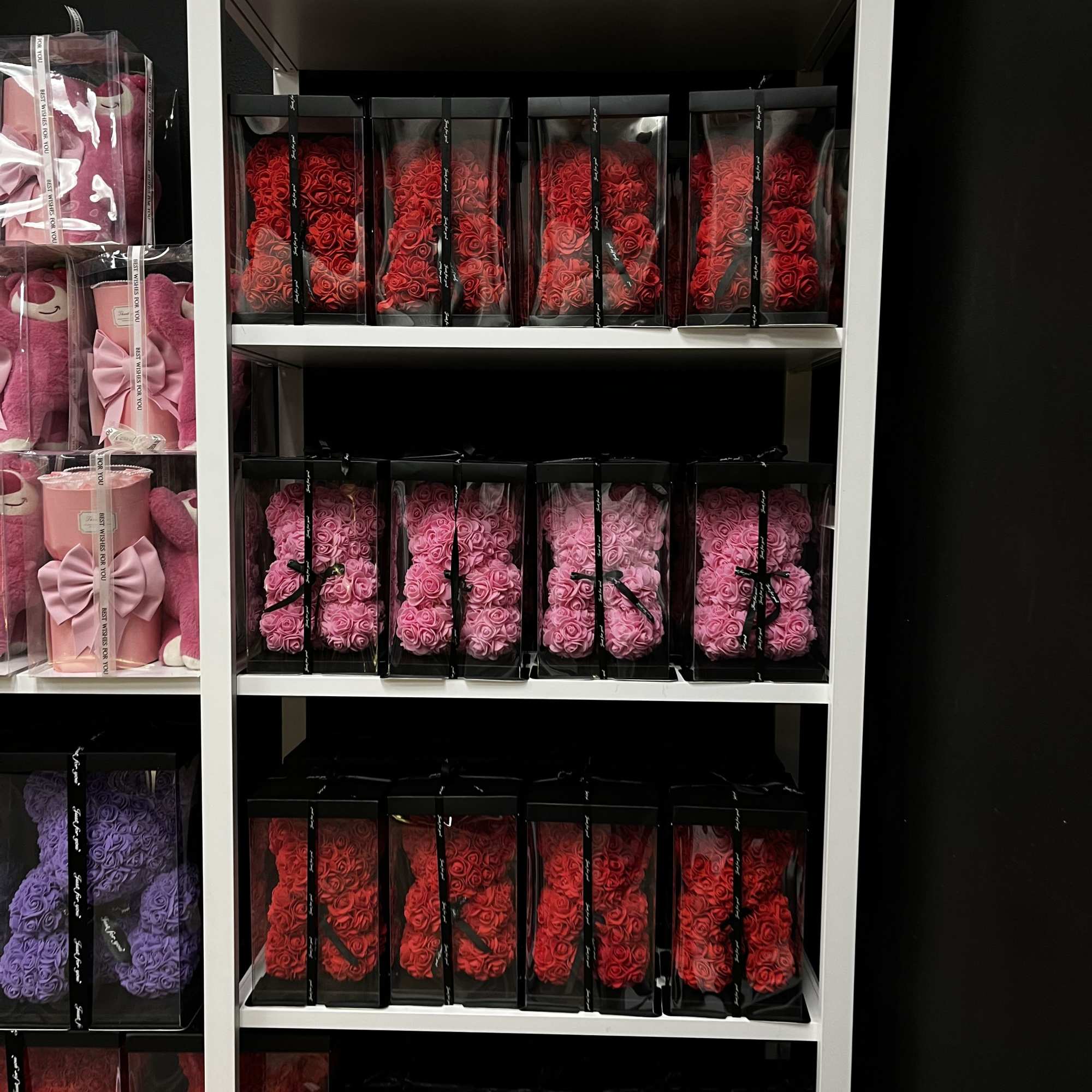 Shelves of boxed rose arrangements in red, pink, purple, and blue.