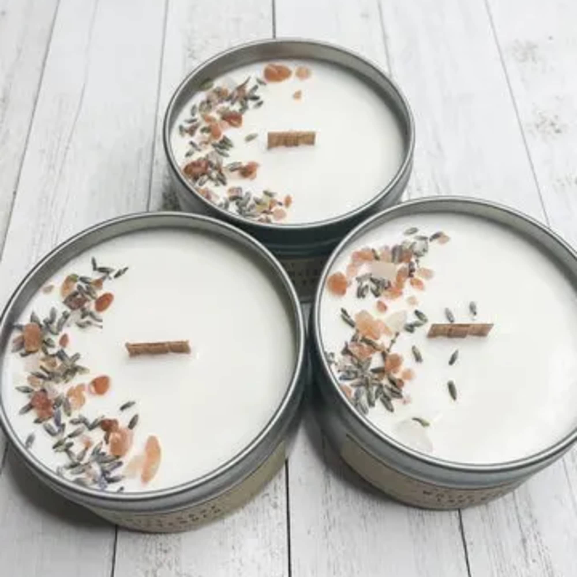 Three white tin candles with wooden wicks and toppings on a white wood surface