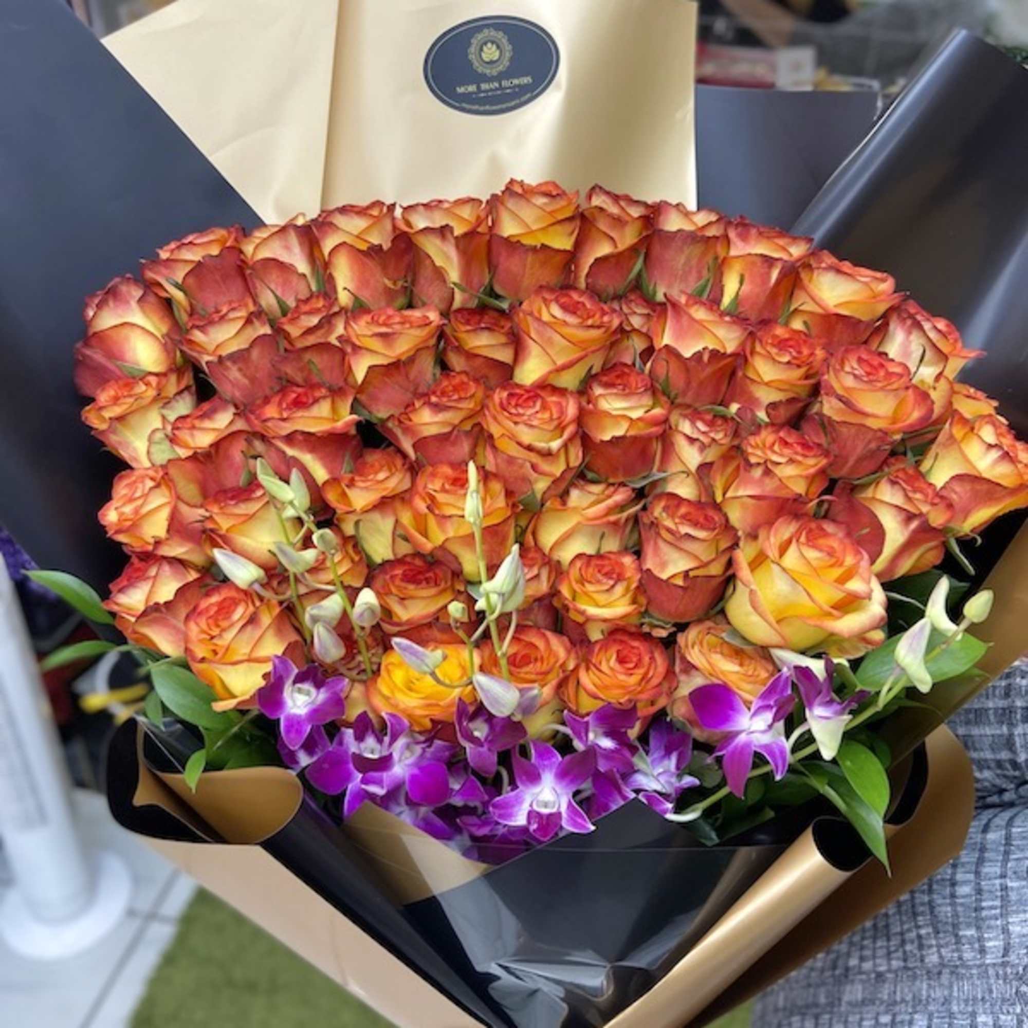 Large bouquet of orange and yellow roses with purple orchids wrapped in black and gold paper