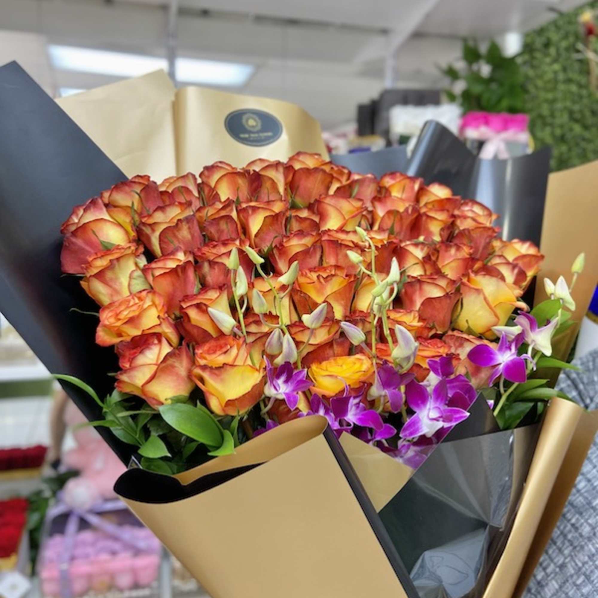 Large bouquet of orange-yellow roses with purple orchids wrapped in black and gold paper