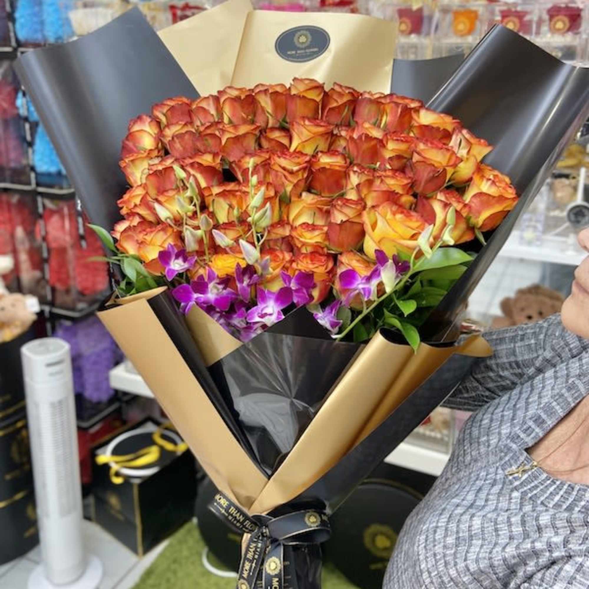 Large bouquet of orange roses with purple orchids wrapped in black and gold paper