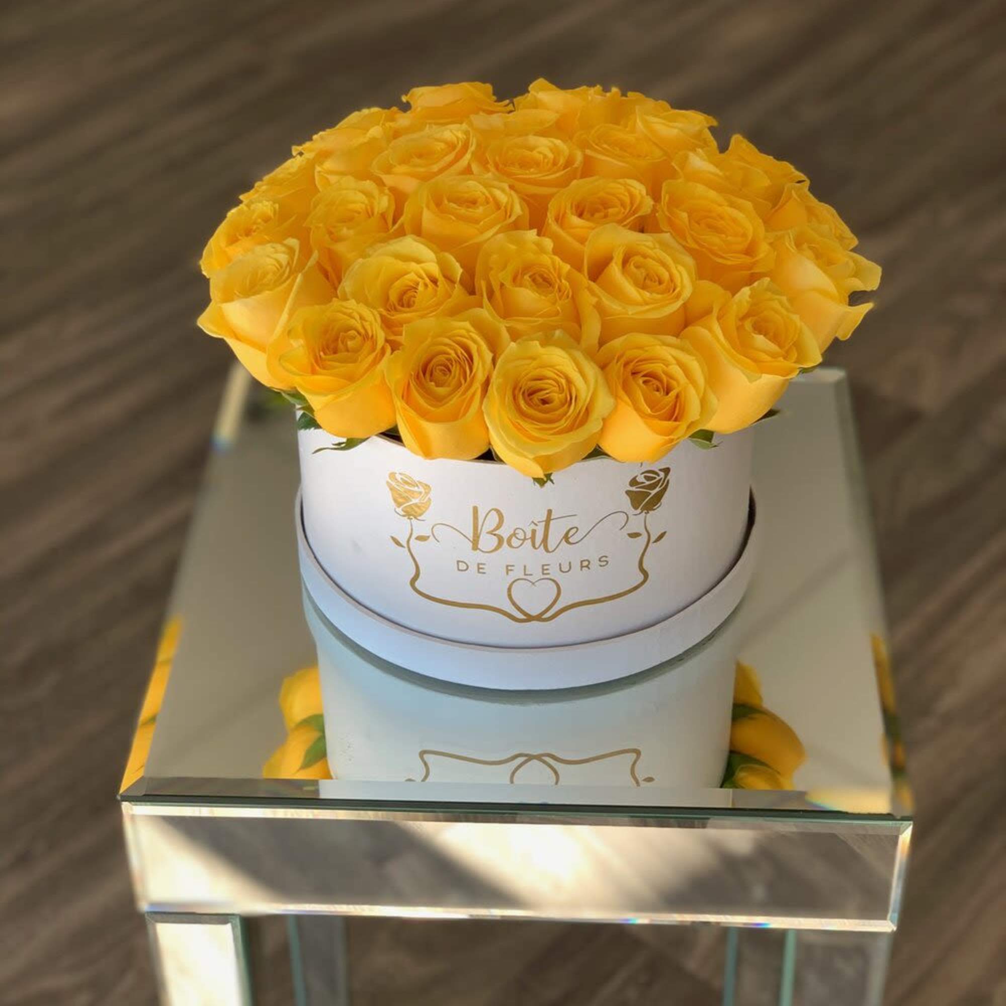 Yellow roses arranged in a round white hat box on a mirrored table