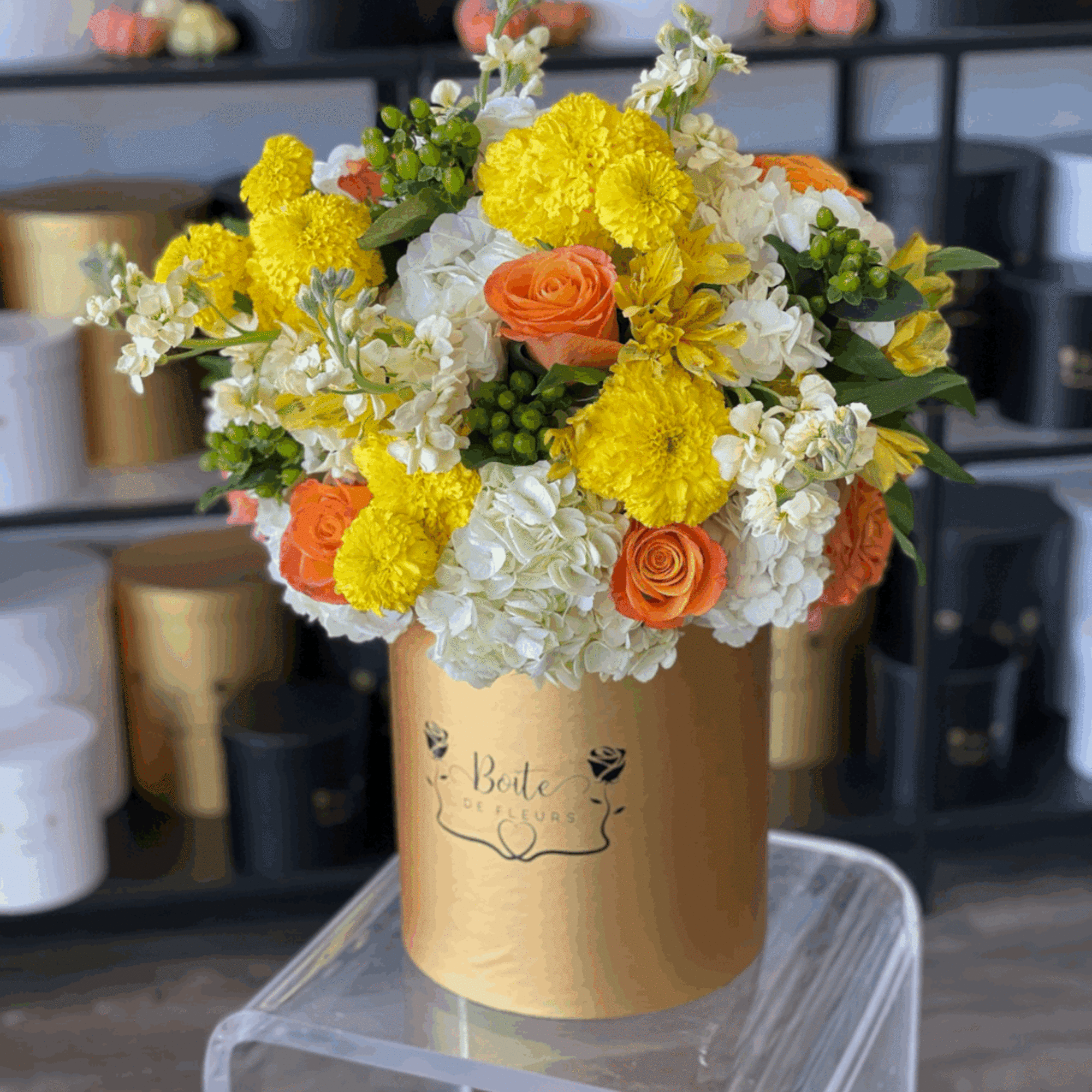 Yellow, white, and orange flower arrangement in a gold hatbox