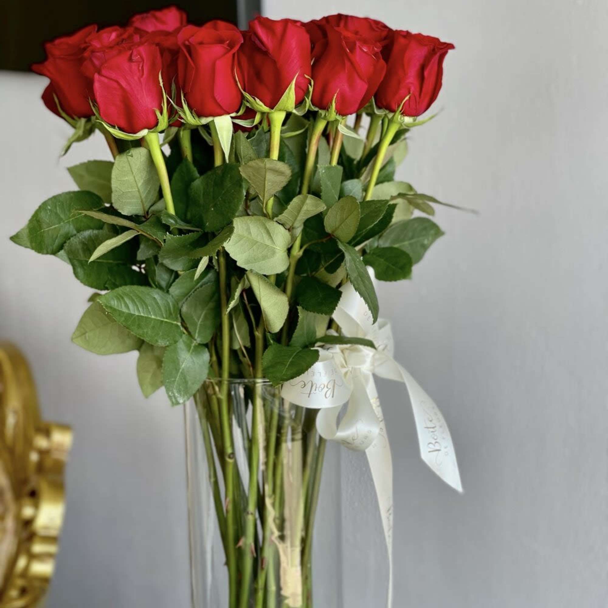 Tall bouquet of red roses in a clear glass vase with a white ribbon