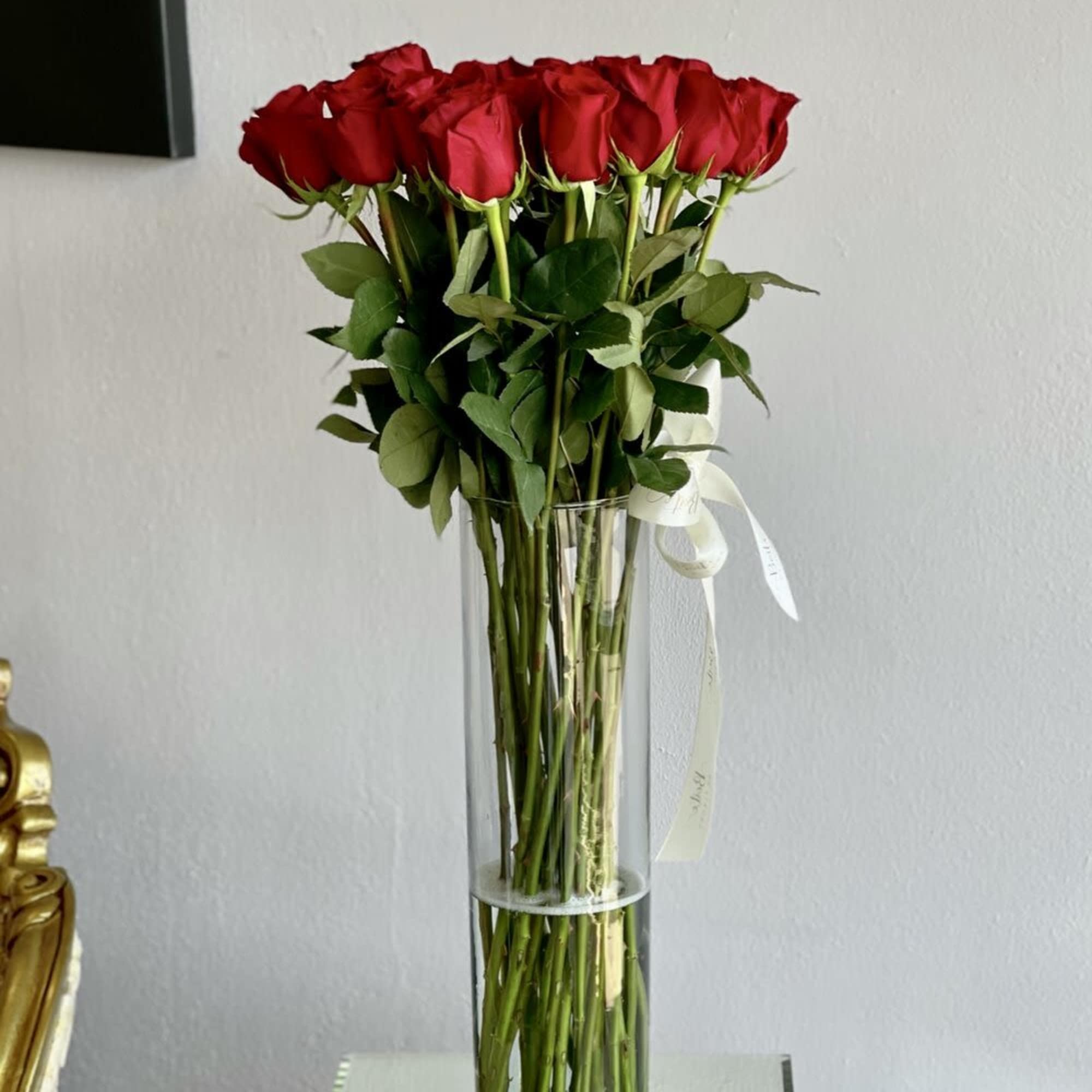 Tall vase of red roses with a white ribbon