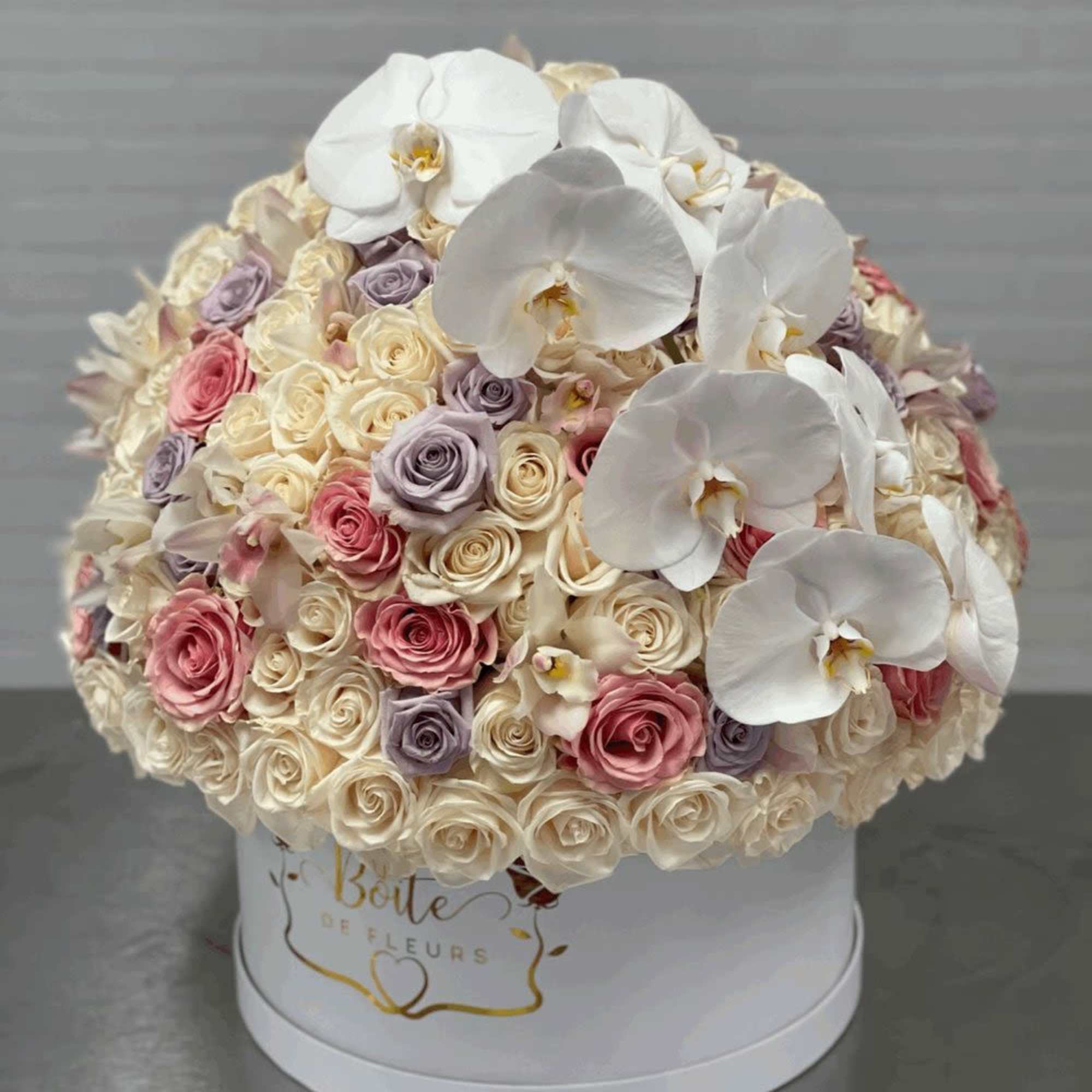 Round bouquet of white orchids and pastel roses in a white hat box