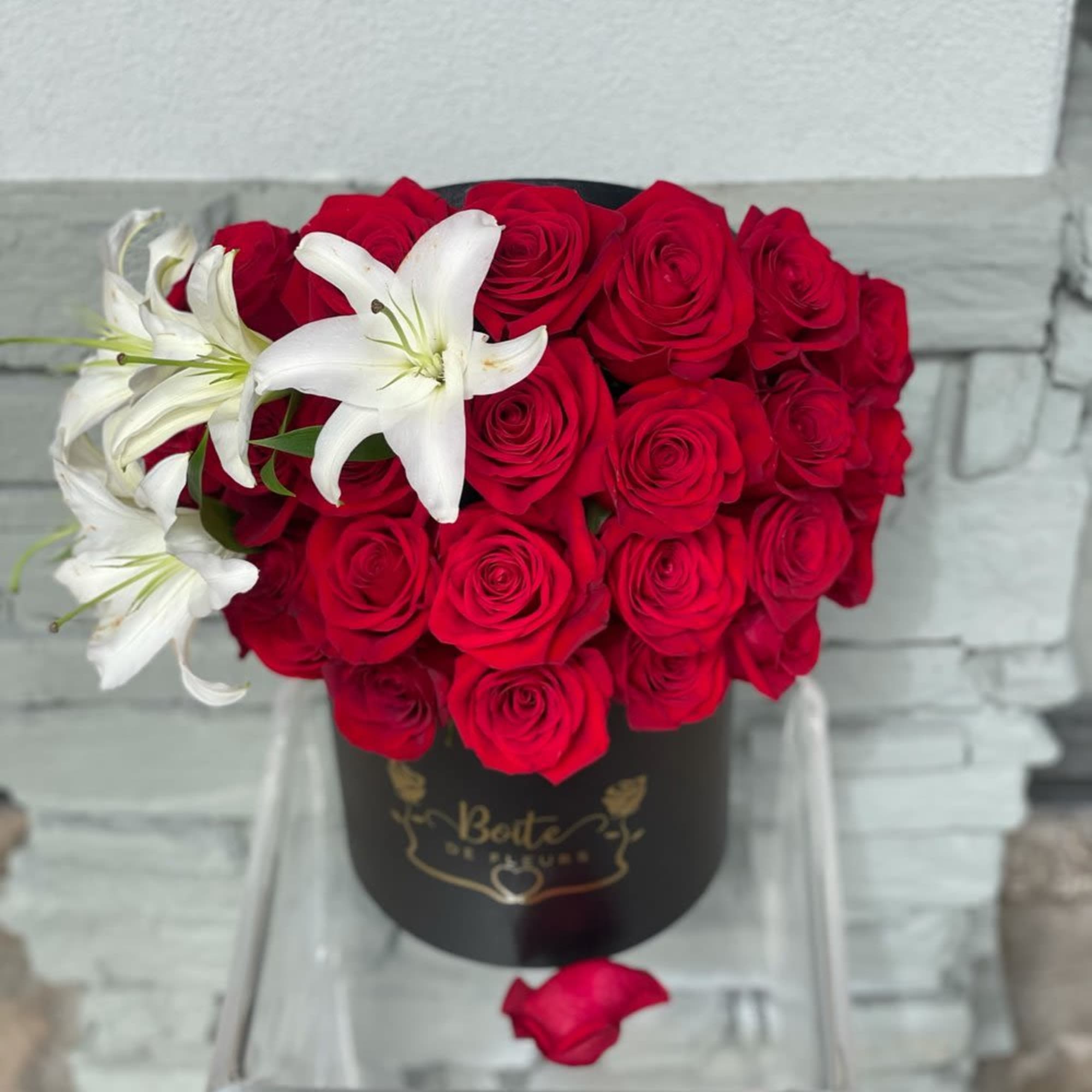 Red roses arranged in a black hat box with white lilies