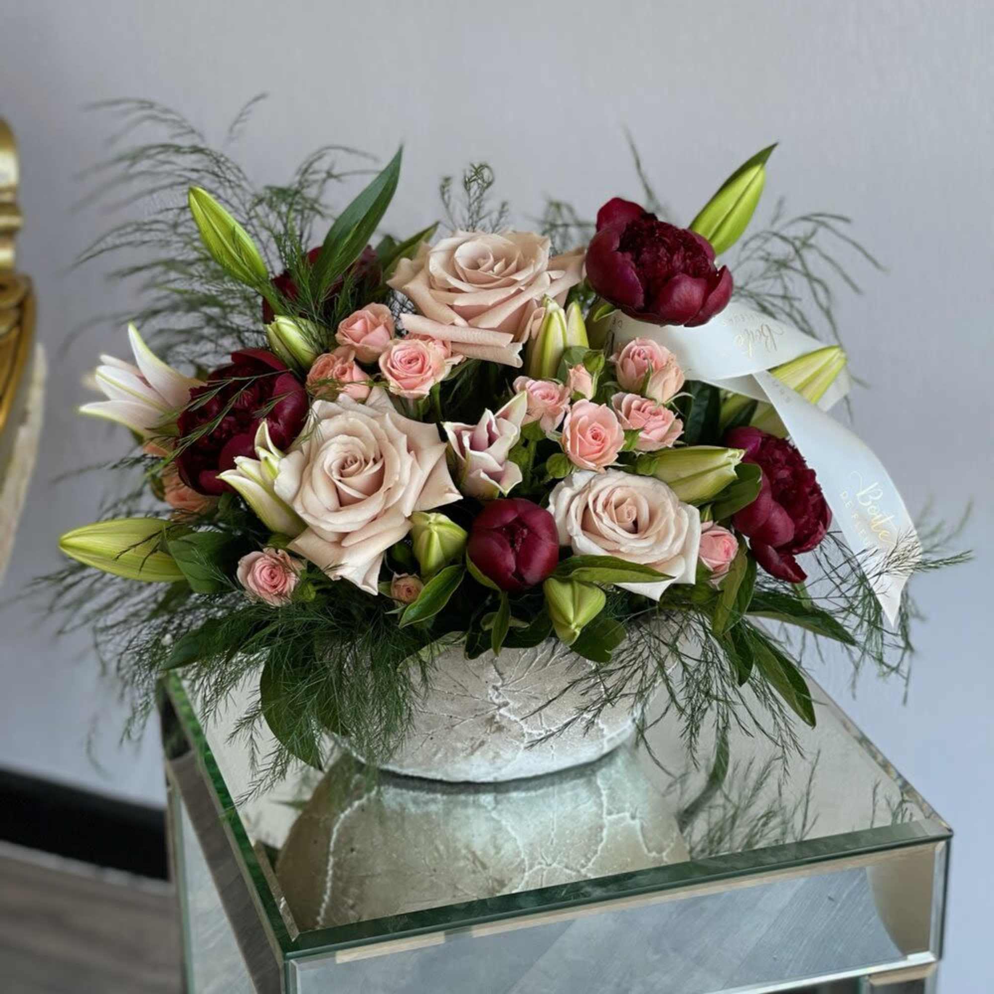 Bouquet of blush roses, burgundy blooms, and lilies in a white vase