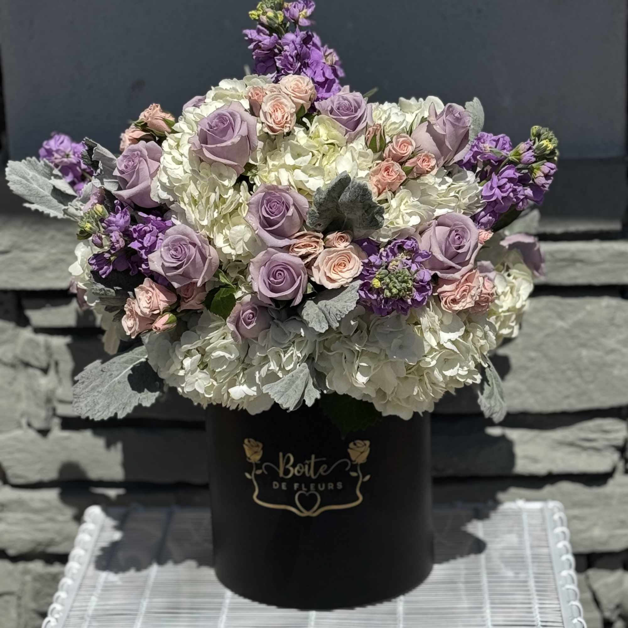 Lavender roses and white hydrangeas in a black hat box