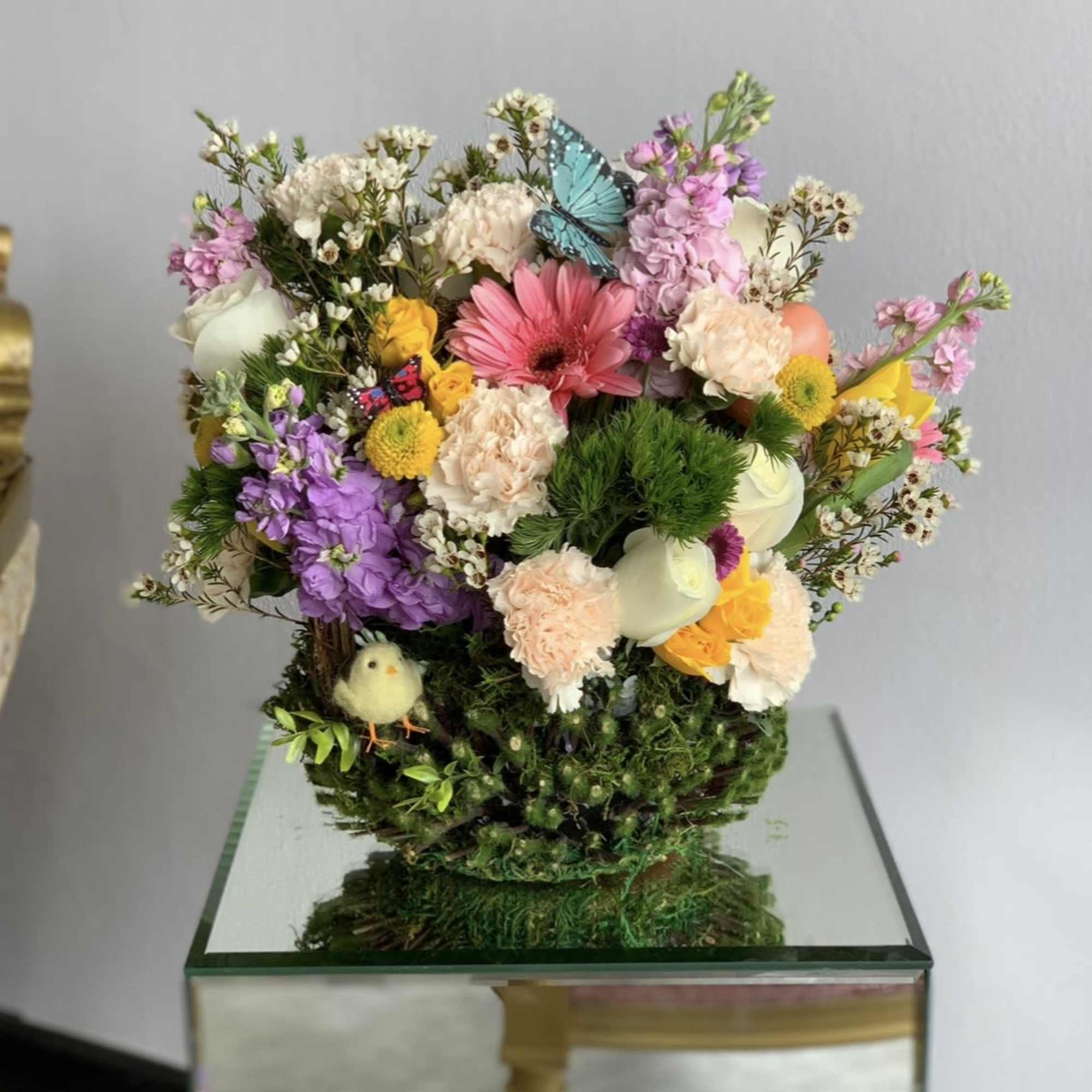 Colorful mixed flower arrangement in a moss-covered container with butterfly accents