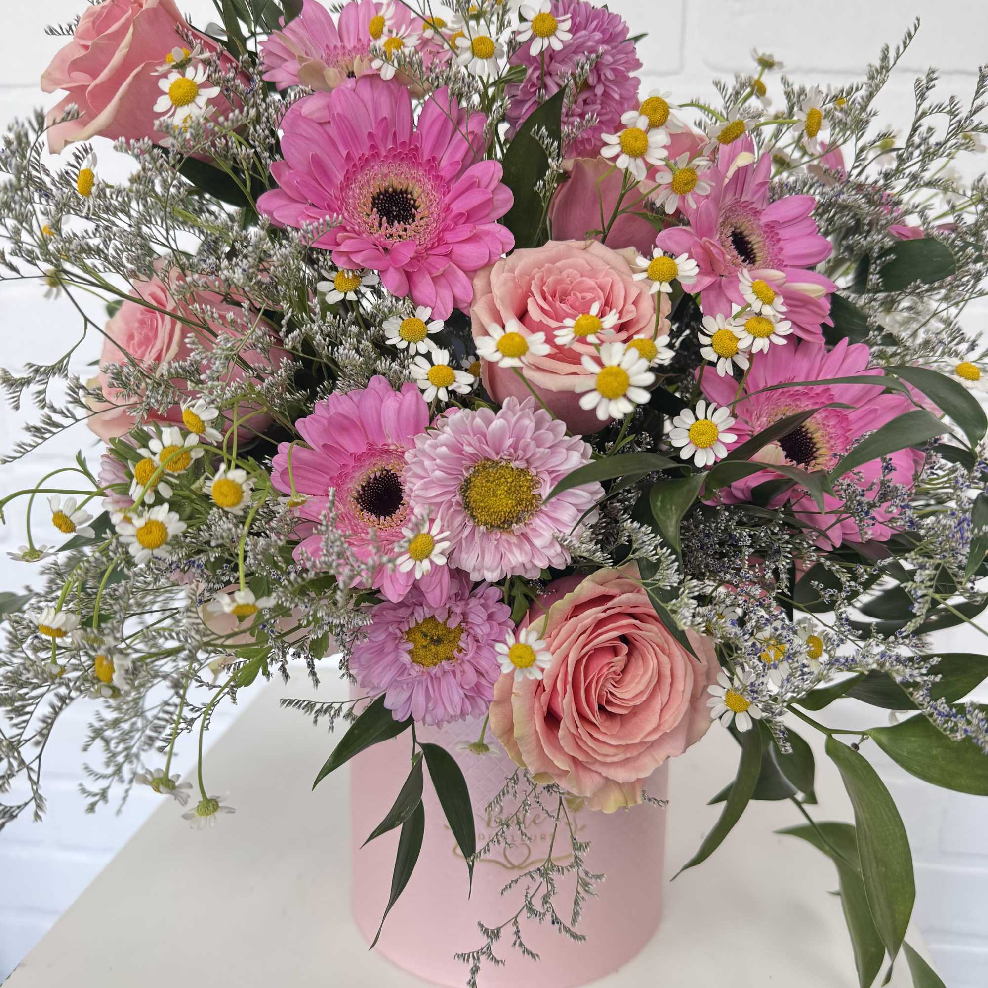 Pink roses and gerbera daisies in a pink hatbox with small white daisies