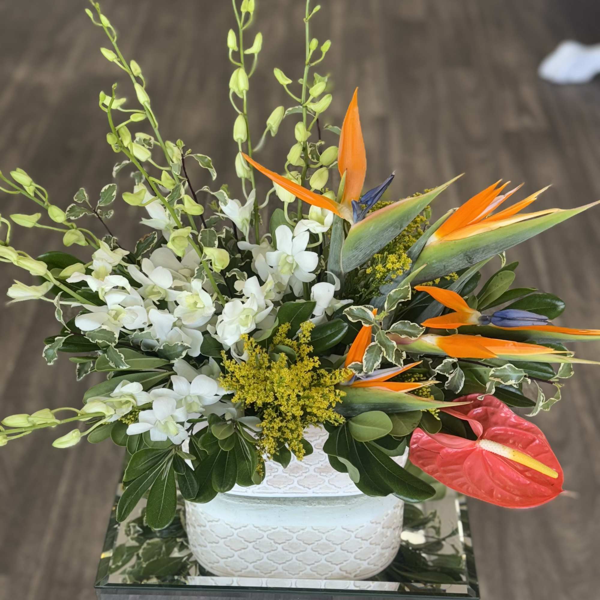 Tropical floral arrangement with white orchids and orange bird-of-paradise in a white vase