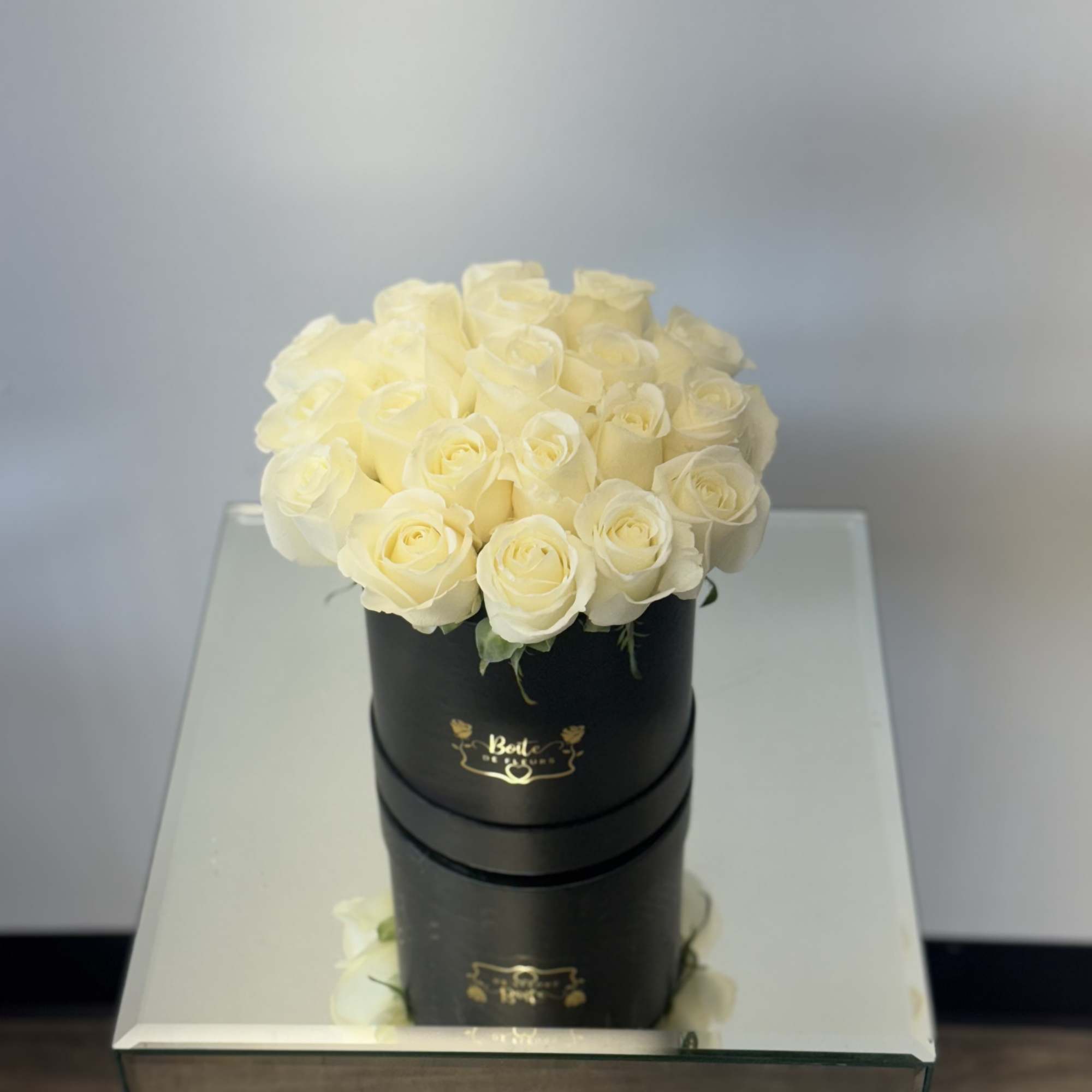 Cream roses arranged in a black round box on a mirrored table