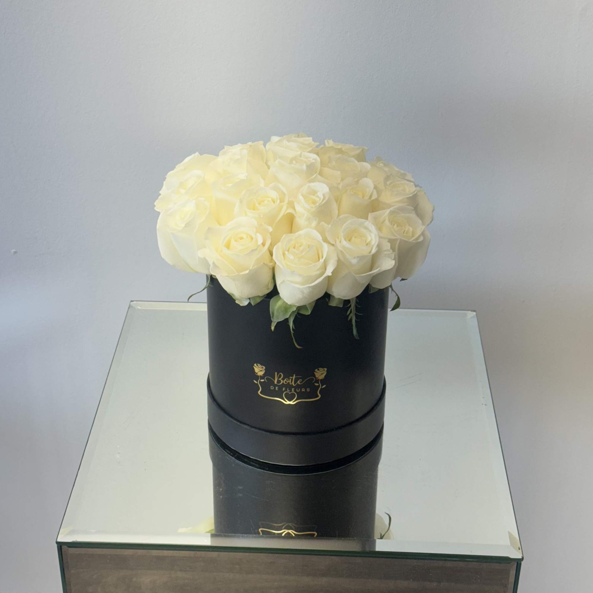 Cream roses arranged in a black round box on a mirrored table