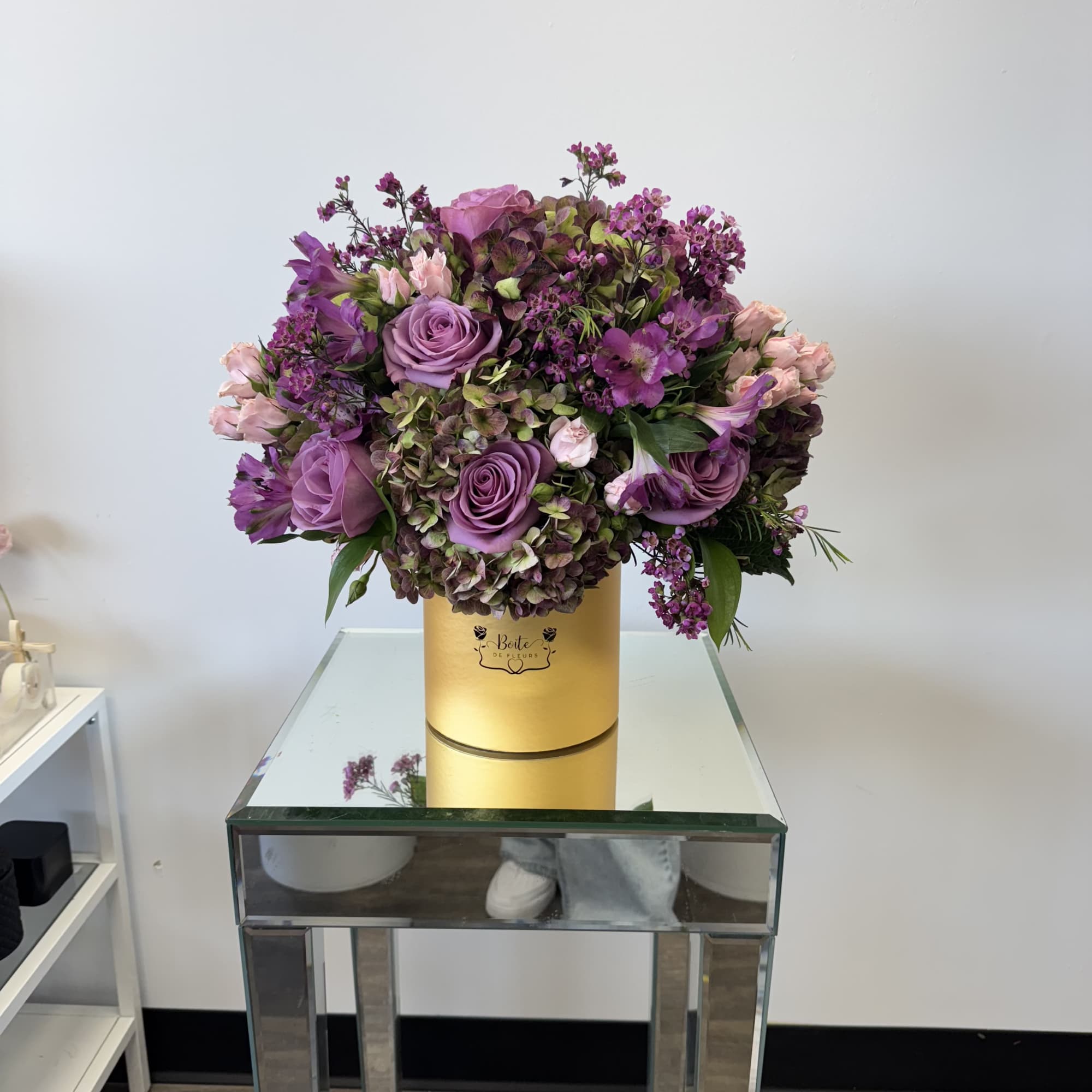 Purple rose bouquet in a gold hatbox on a mirrored table