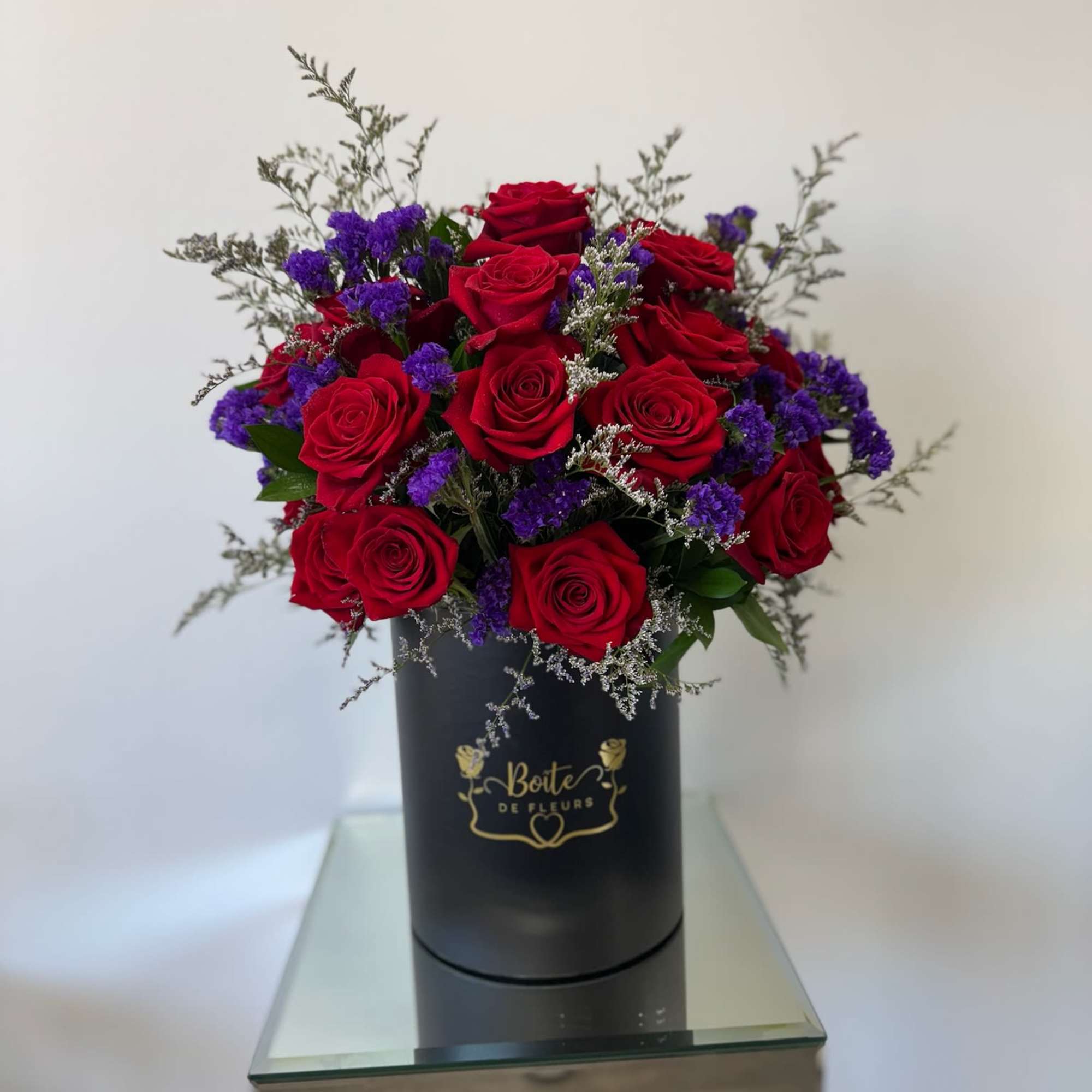 Red roses and purple filler flowers in a black hat box