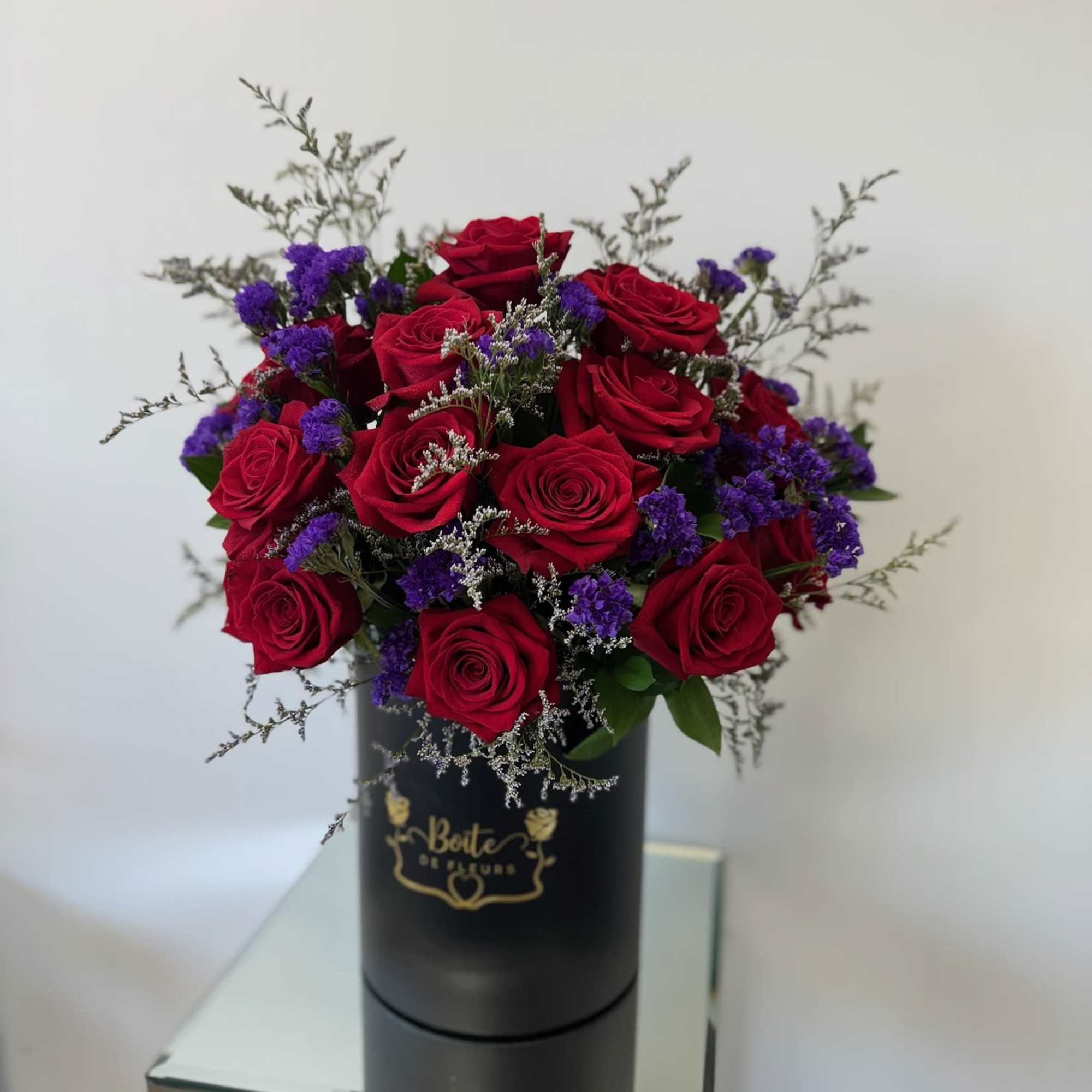 Red roses and purple filler flowers in a black hatbox