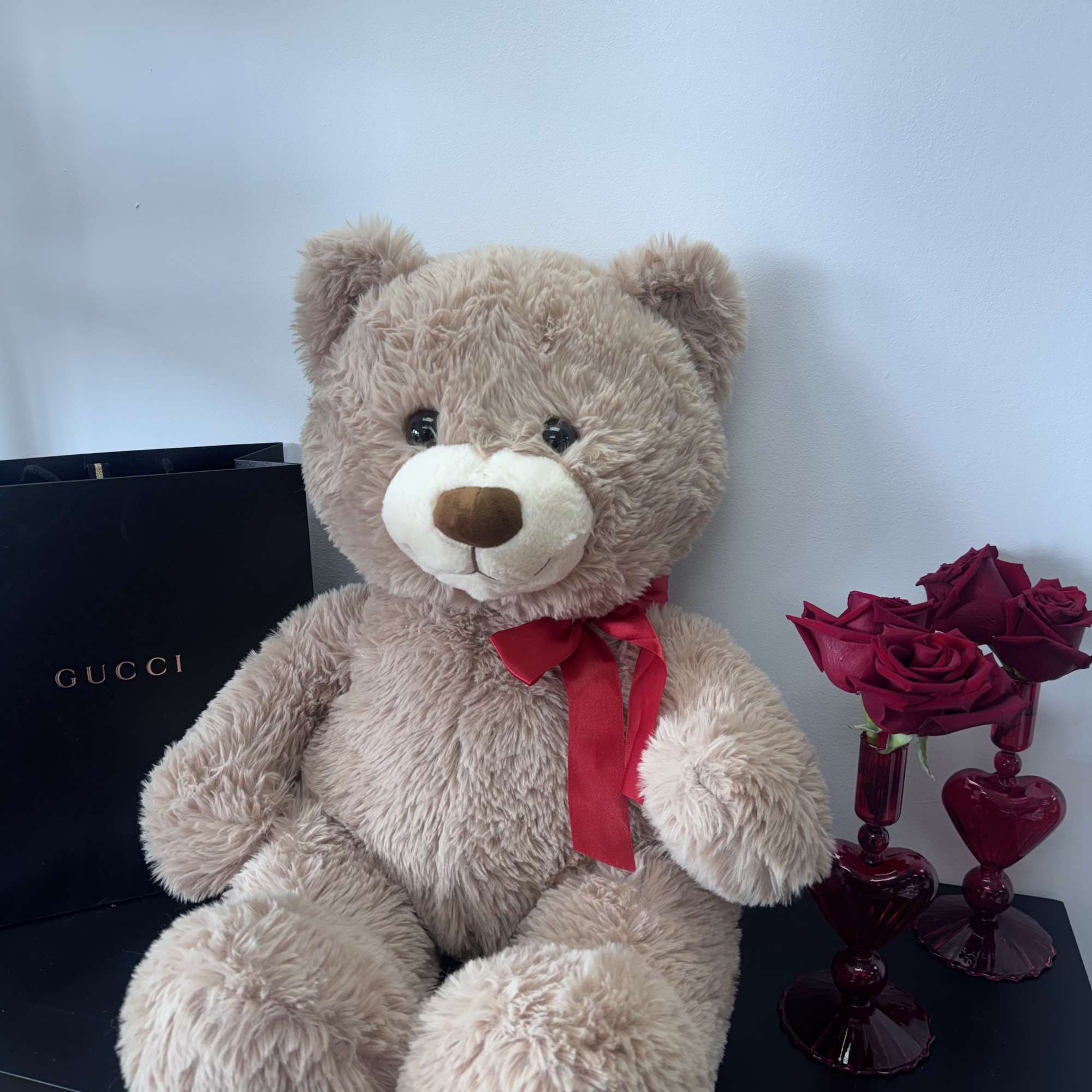 Teddy bear with a red ribbon beside a small vase of red roses