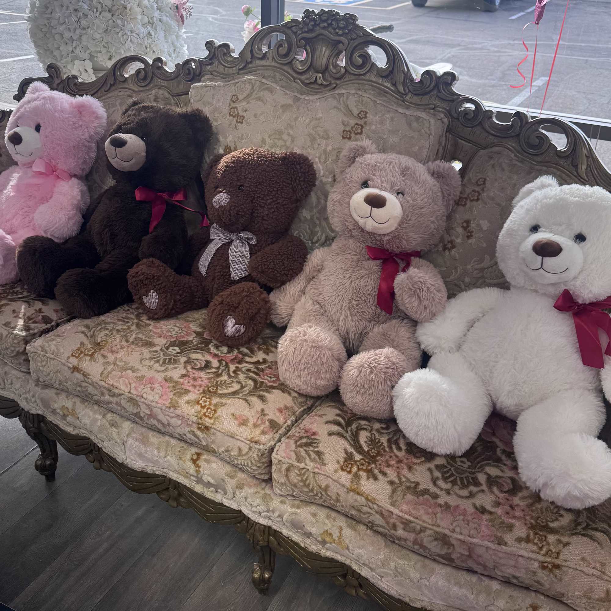 Five teddy bears sit on an ornate floral sofa.