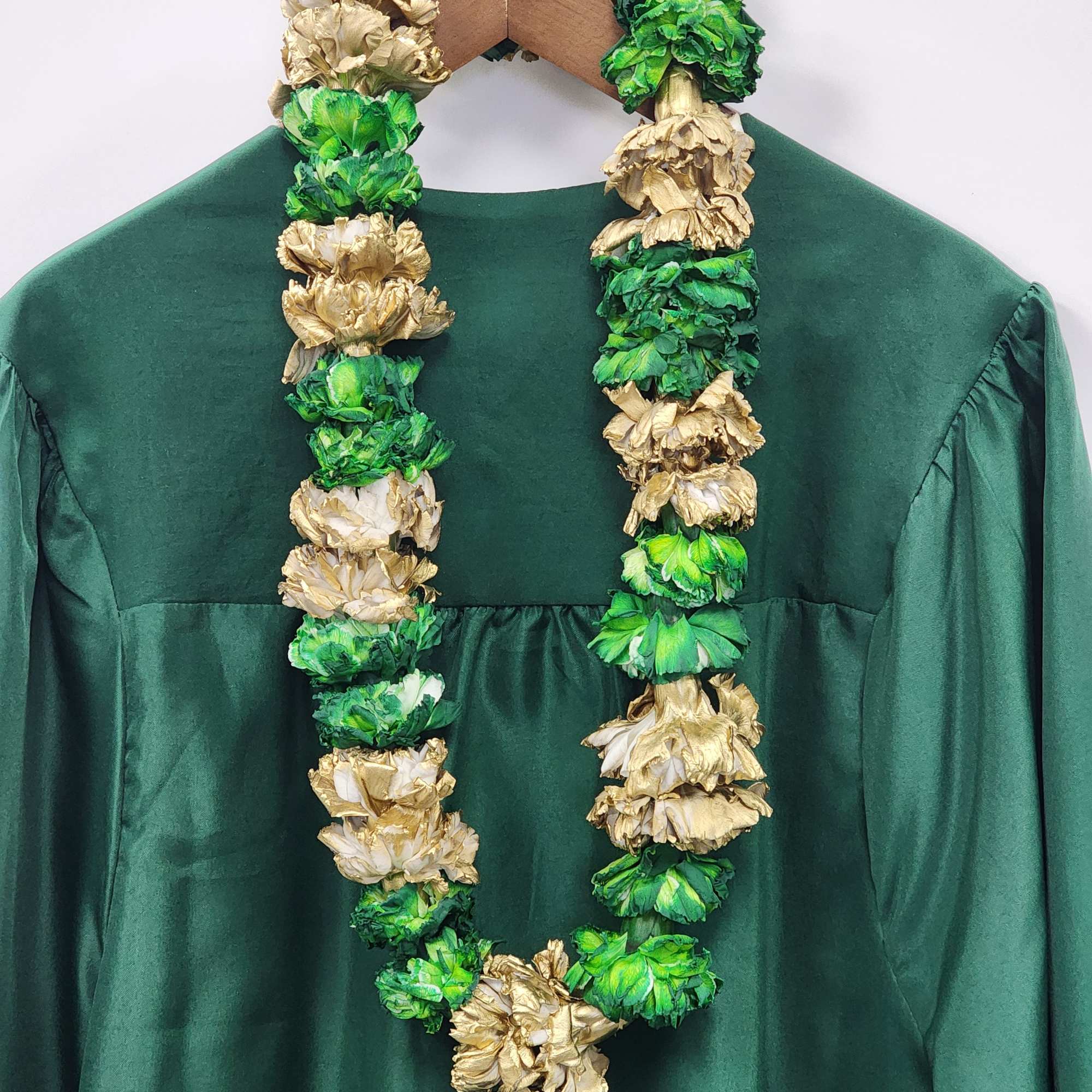 Green and gold floral lei draped over a dark green dress on a hanger