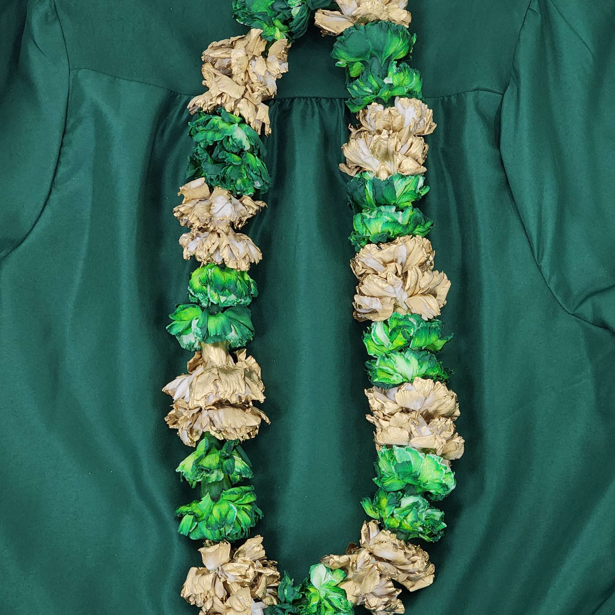 A green and gold flower lei laid on dark green fabric