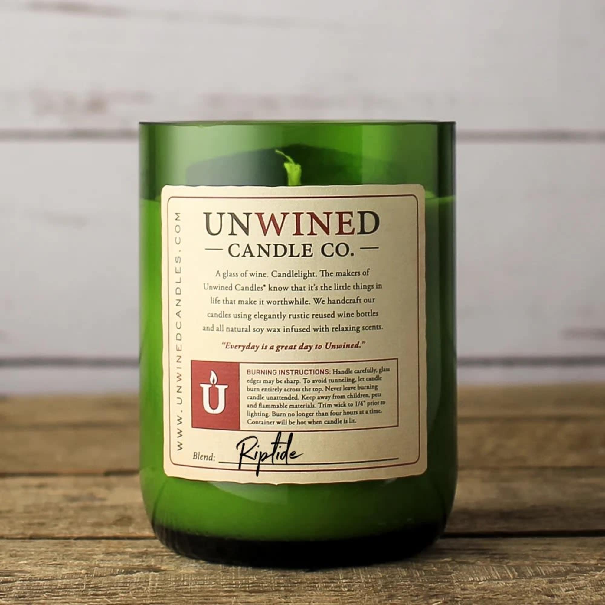 Green glass jar candle with cream label reading Unwined Candle Co. on a rustic wooden surface