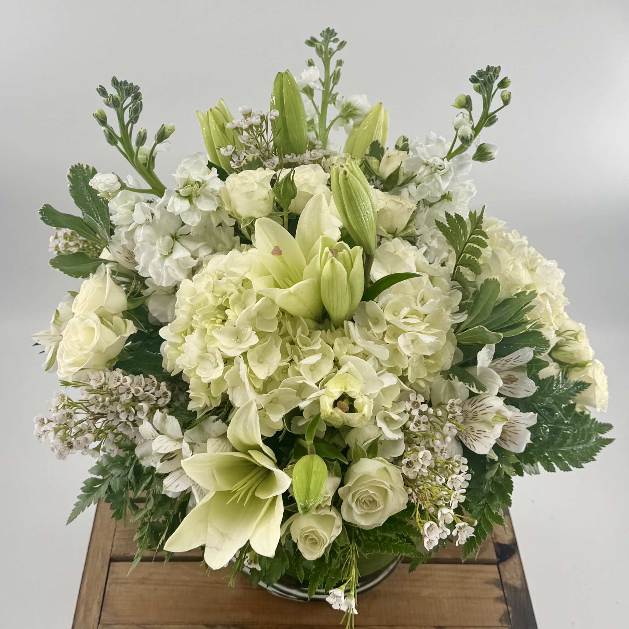 White floral arrangement with lilies, roses, and hydrangeas in a low vase