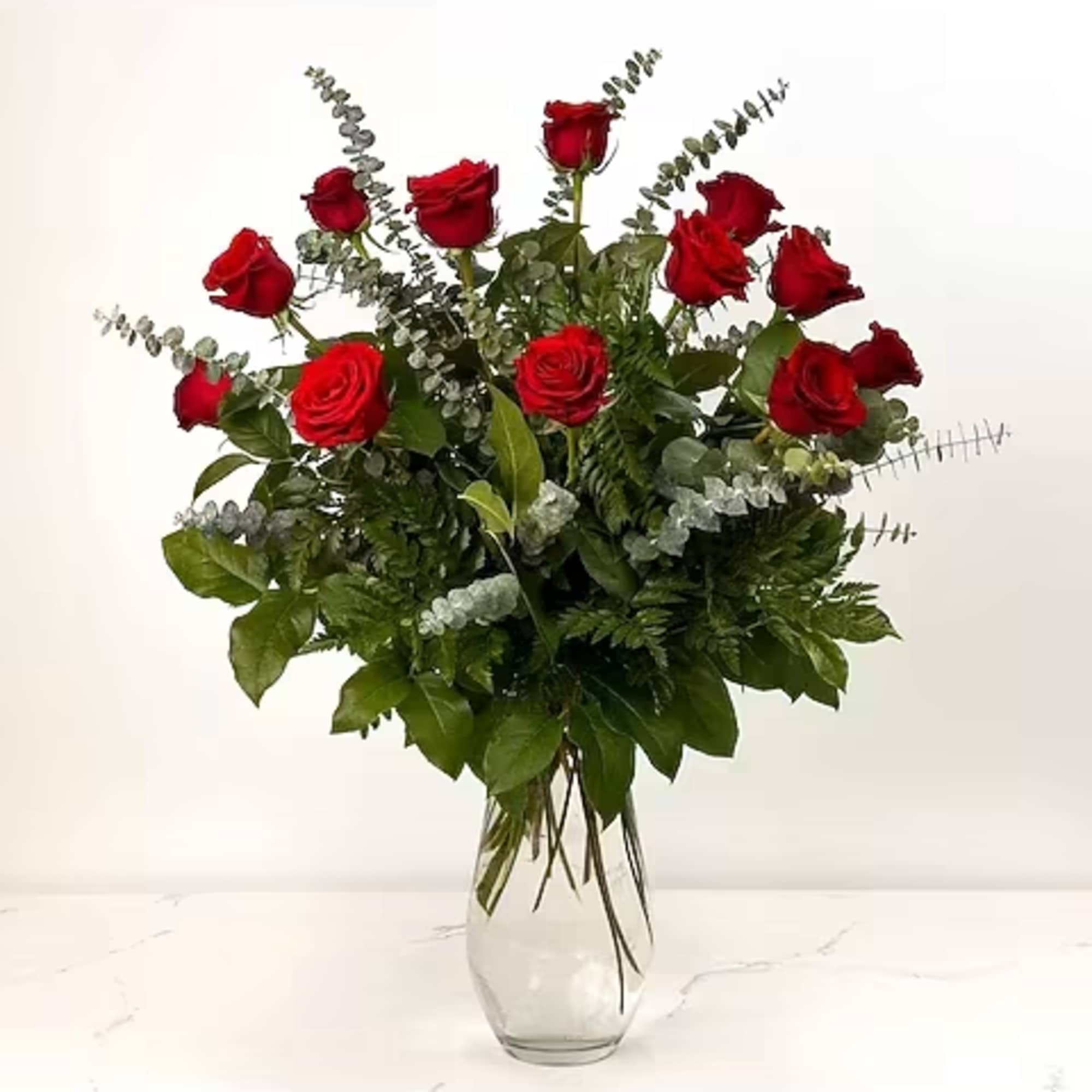 Red roses arranged in a clear glass vase with eucalyptus