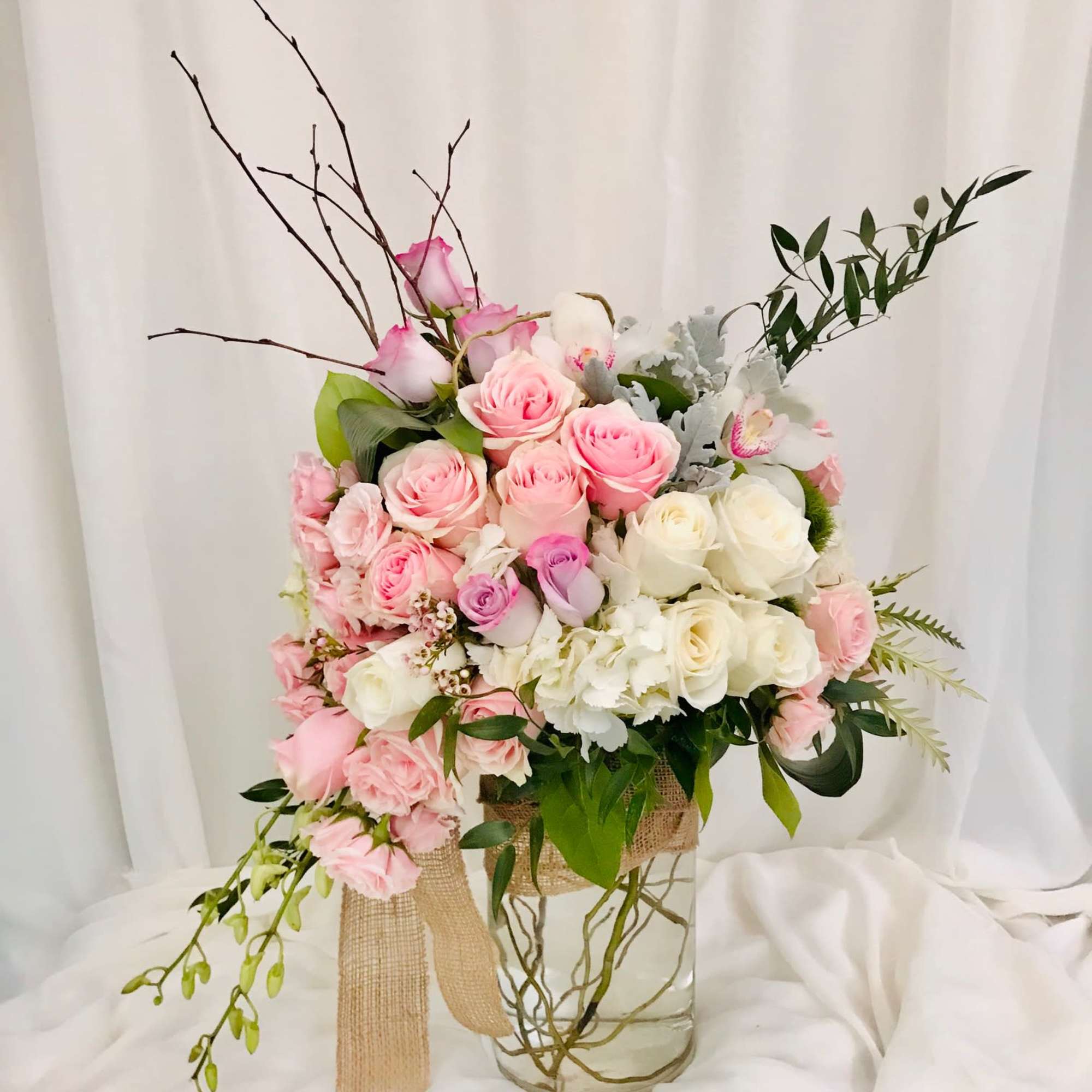 Pink and white rose arrangement in a clear glass vase with ribbon