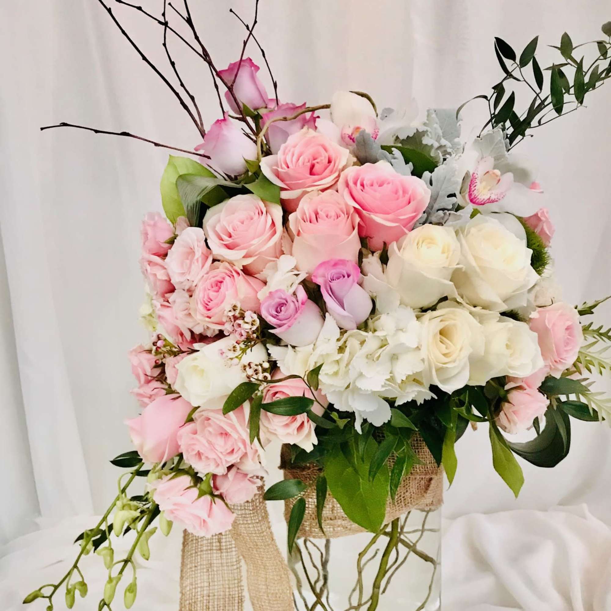 Pink and white rose arrangement in a clear glass vase with burlap ribbon