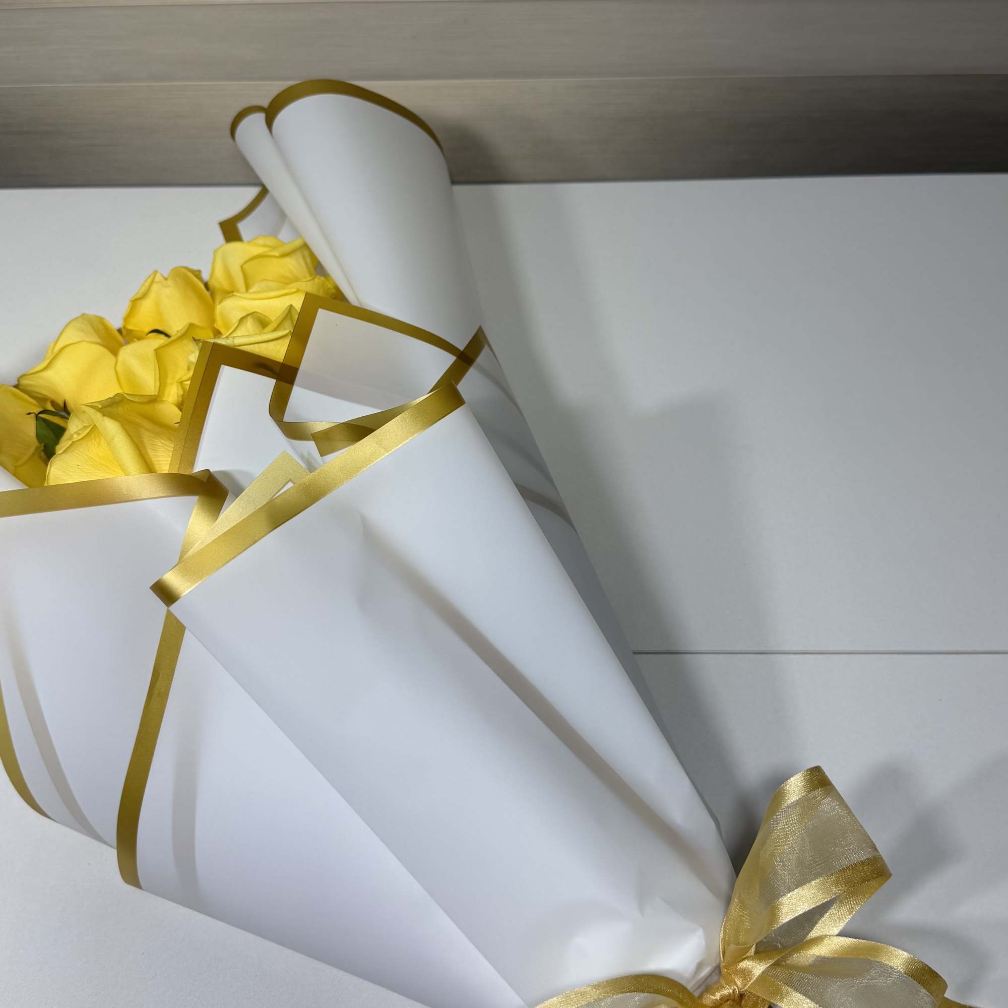 Bouquet of yellow roses wrapped in white paper with gold ribbon