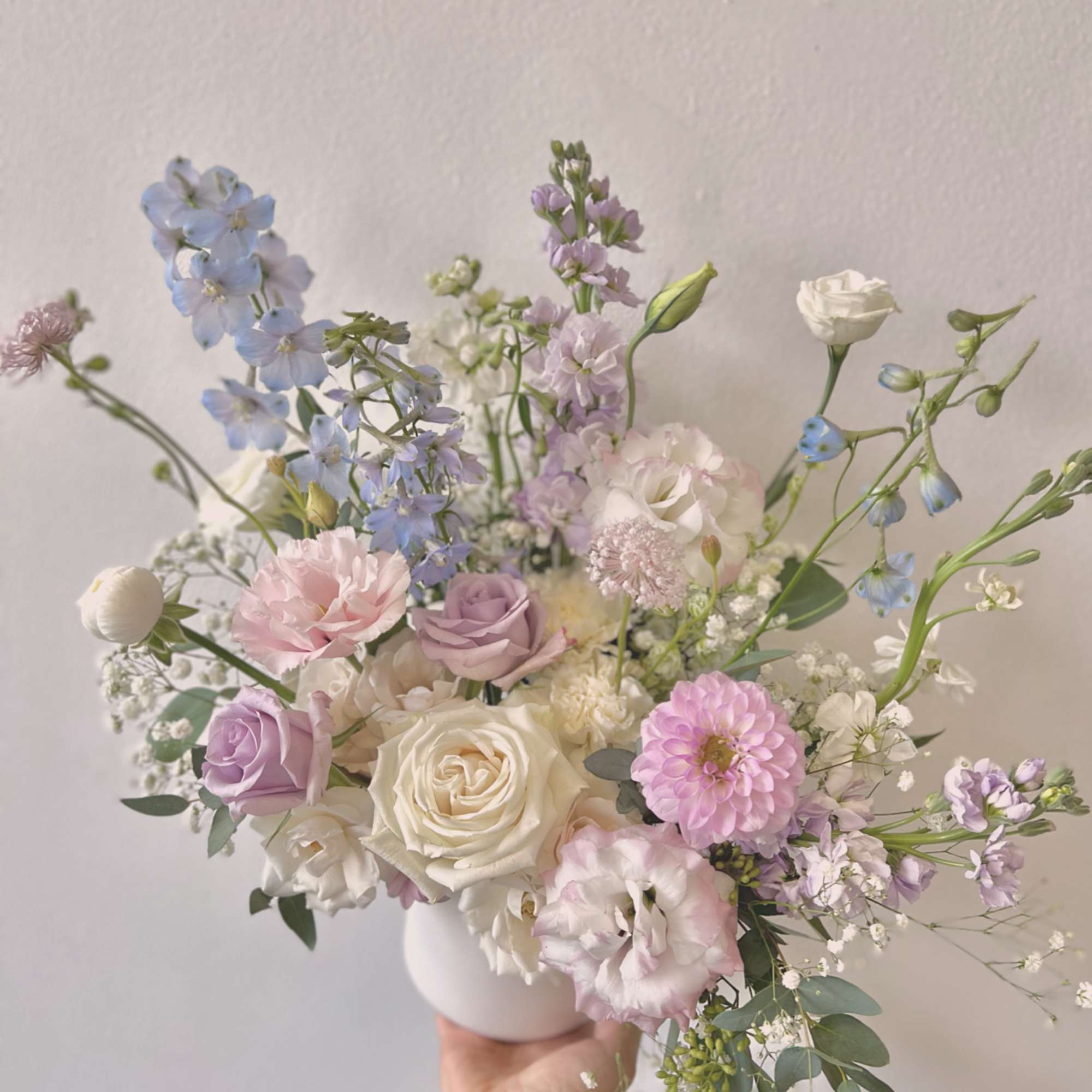Pastel bouquet of roses, lisianthus, and blue delphinium in a white vase