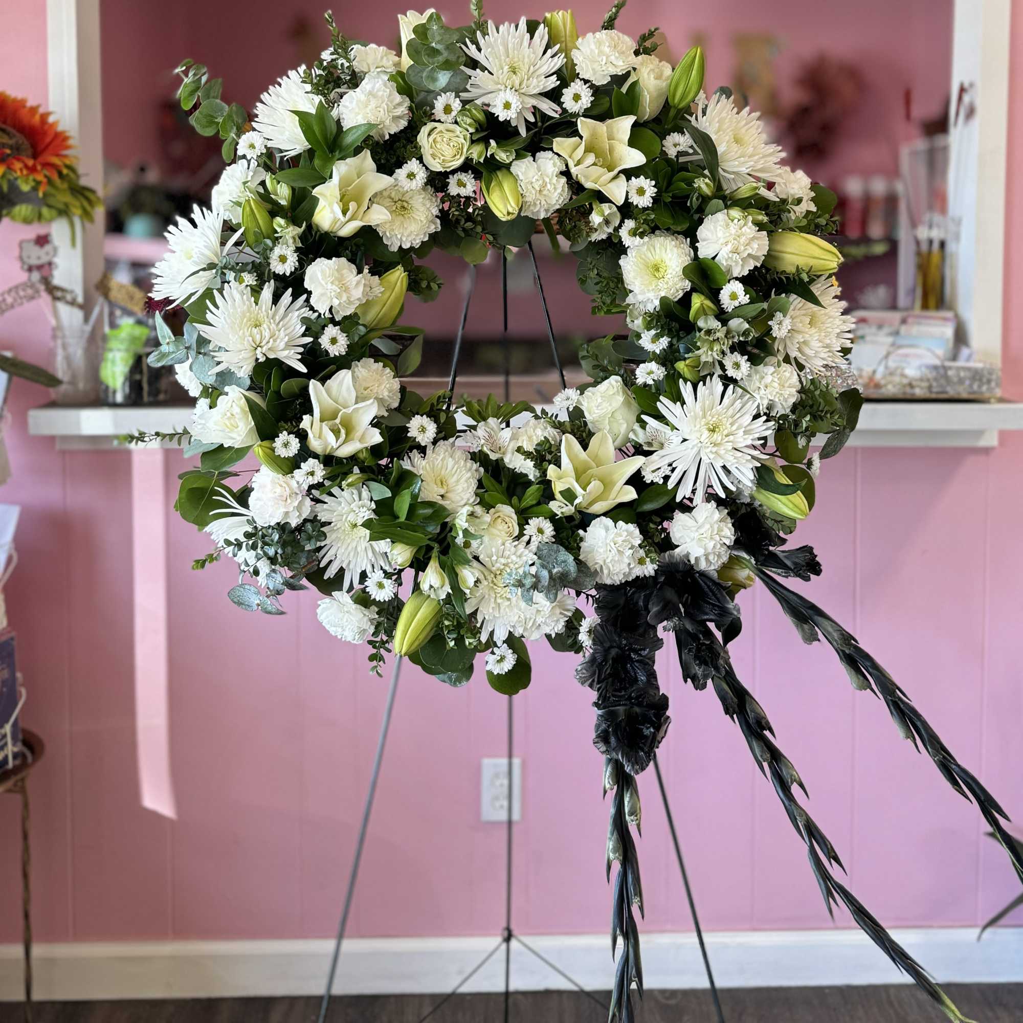 White floral wreath on a stand with black ribbon streamers