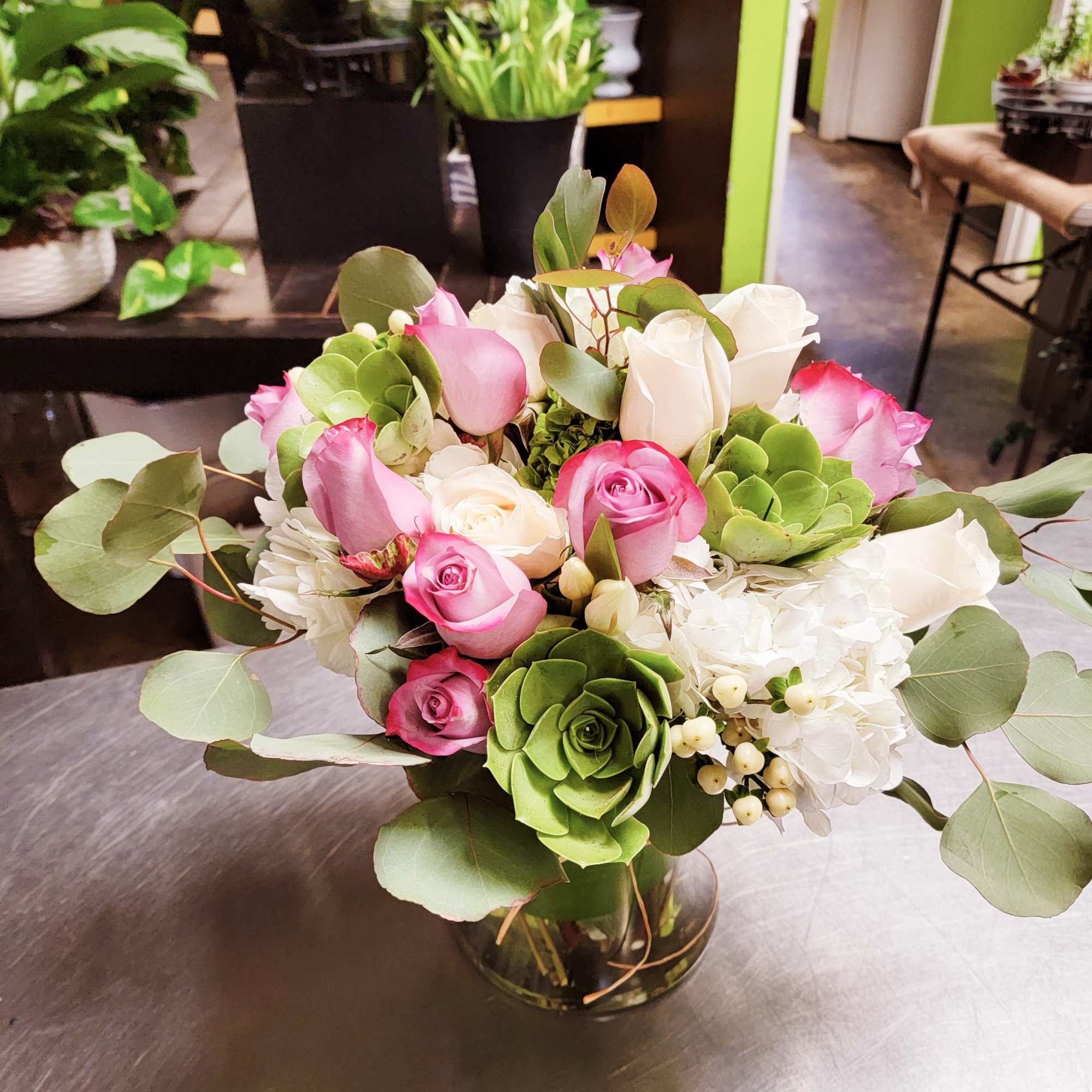 Pink and white roses arranged in a glass vase with eucalyptus