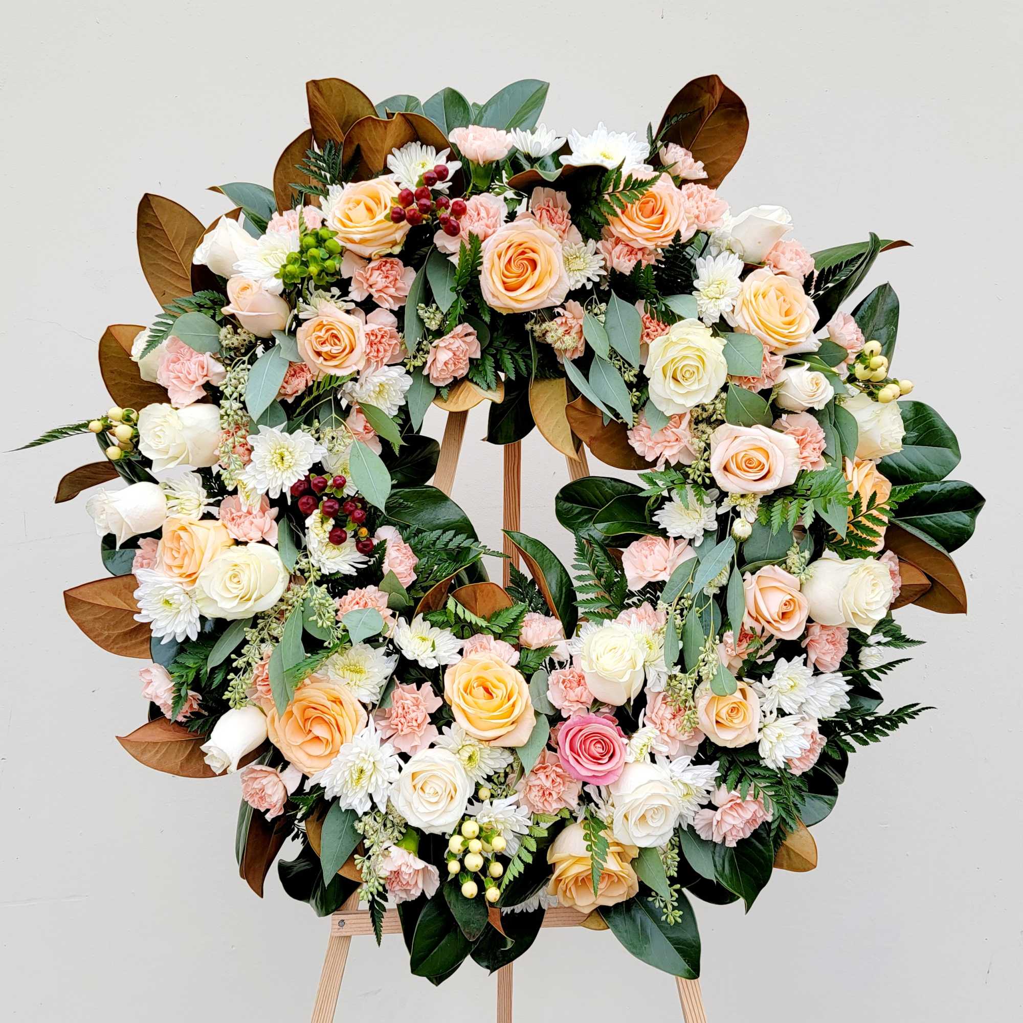 Large floral wreath of roses, carnations, and white daisies on an easel