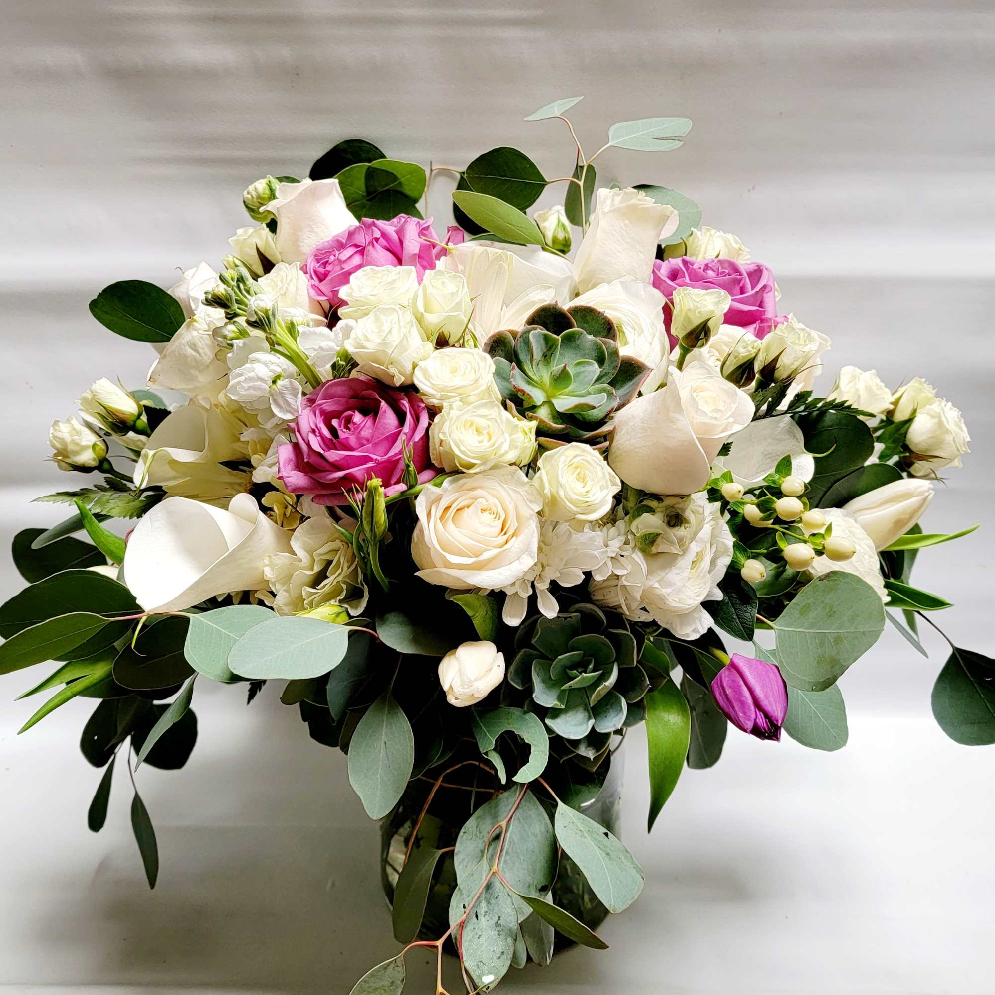 Bouquet of white and pink roses with calla lilies and a succulent in a glass vase