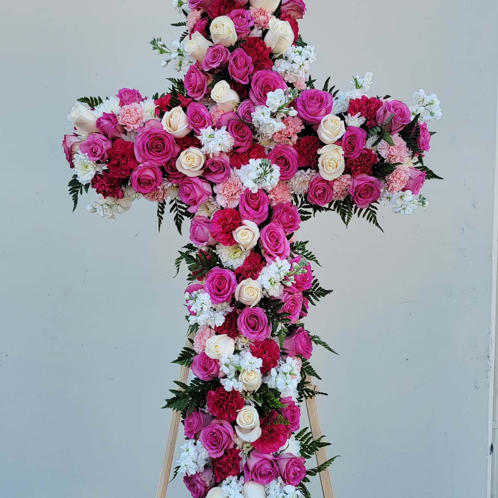 Cross-shaped floral arrangement of pink, white, and red roses on a stand