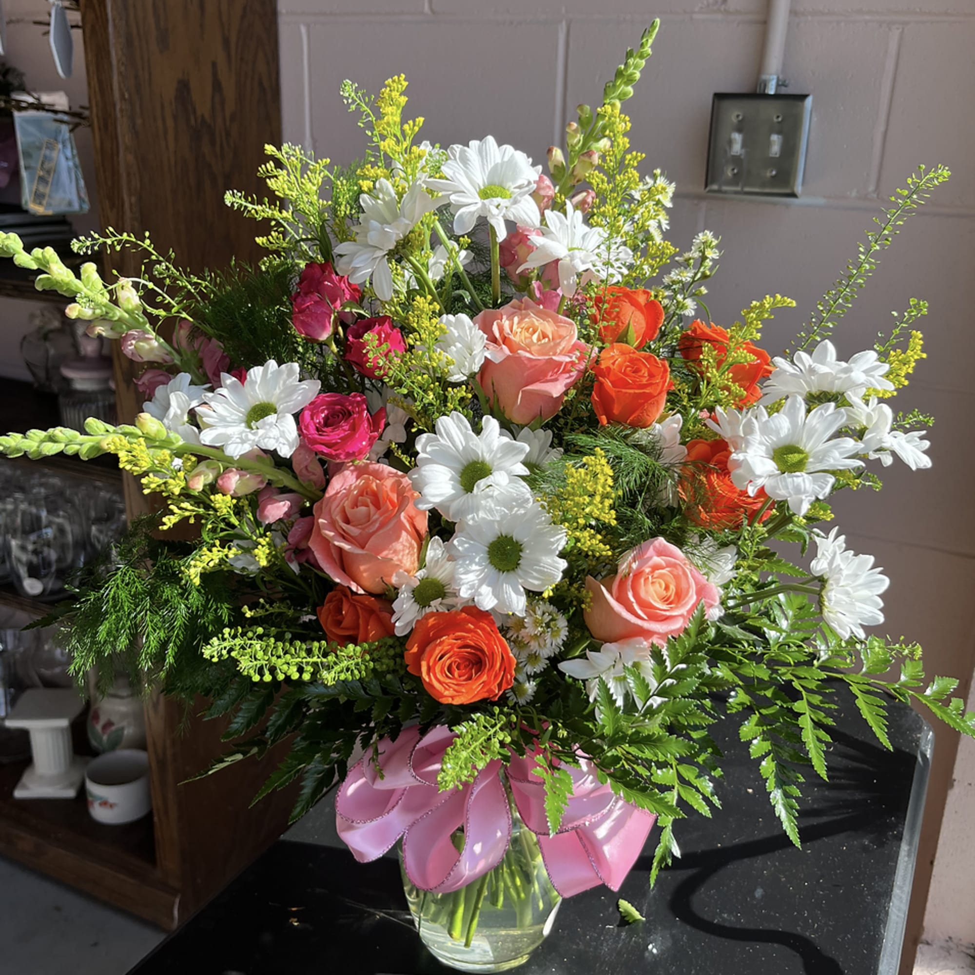 Bouquet of roses and white daisies in a glass vase with a pink ribbon