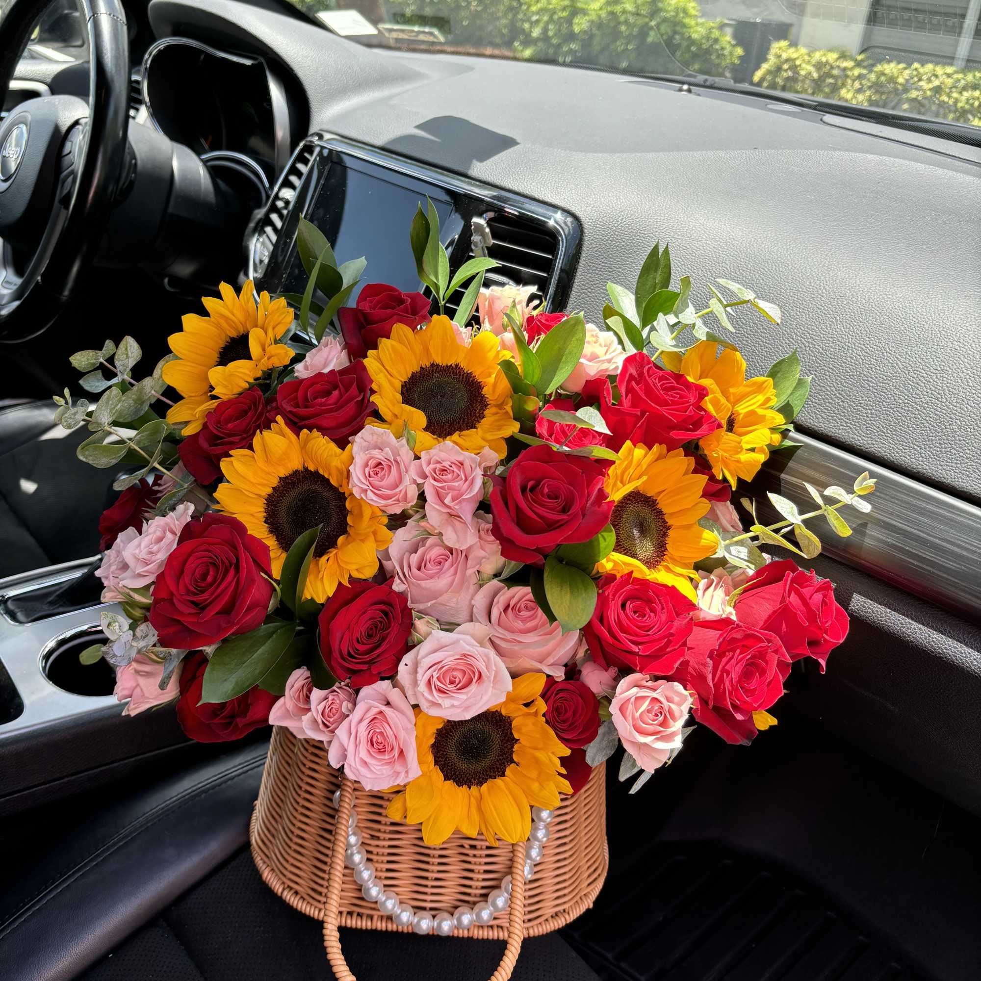 Basket arrangement of red and pink roses with sunflowers in a car seat