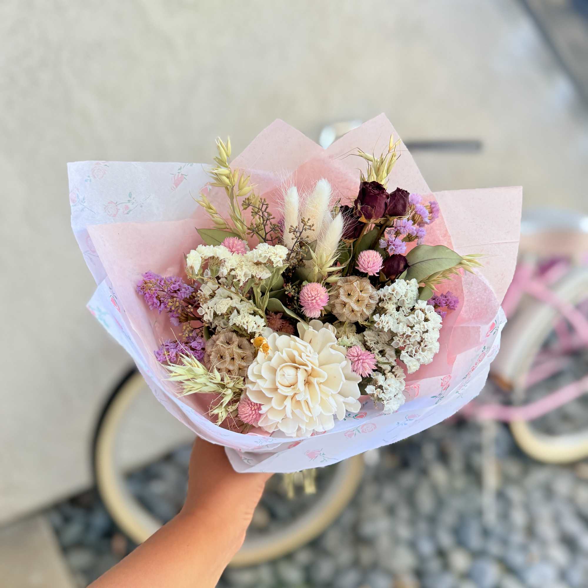 Handheld bouquet of pastel dried flowers wrapped in pink paper