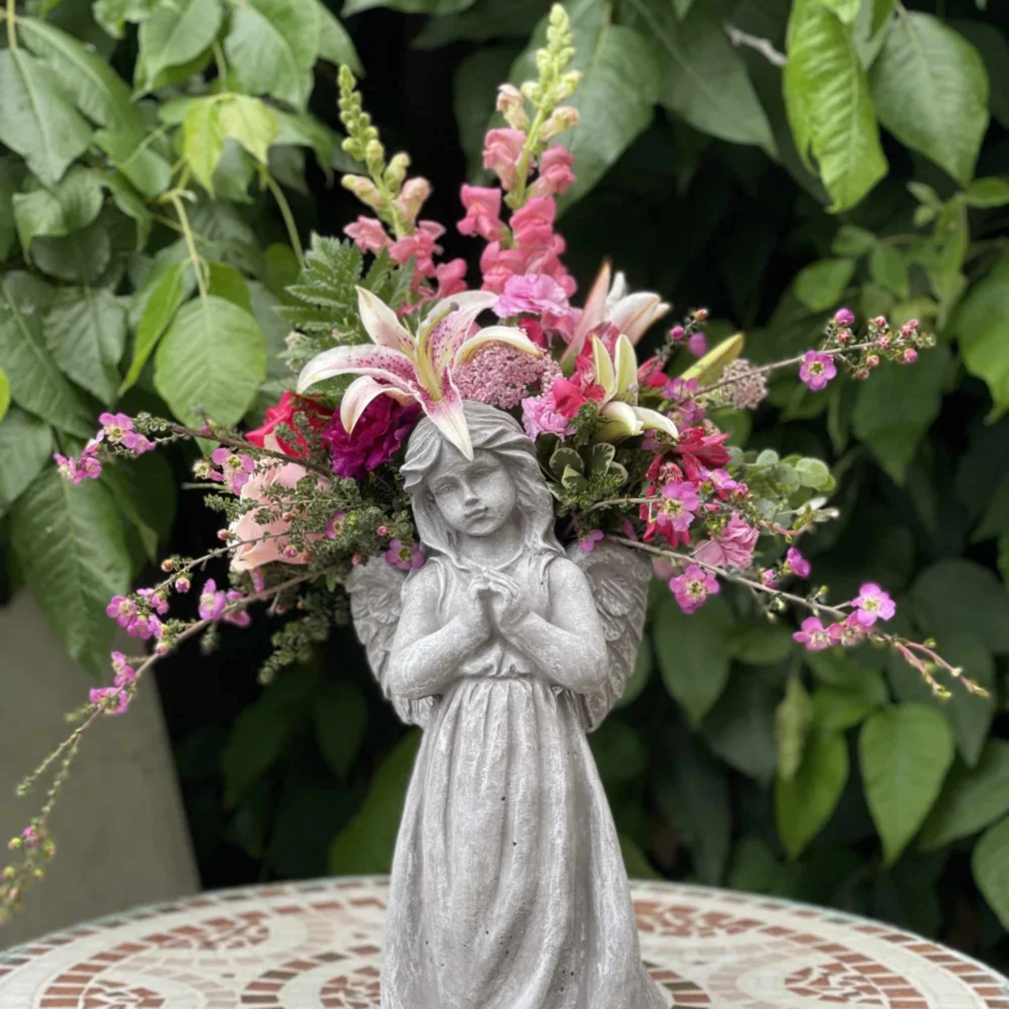 Angel statue with pink and white flowers arranged around its head