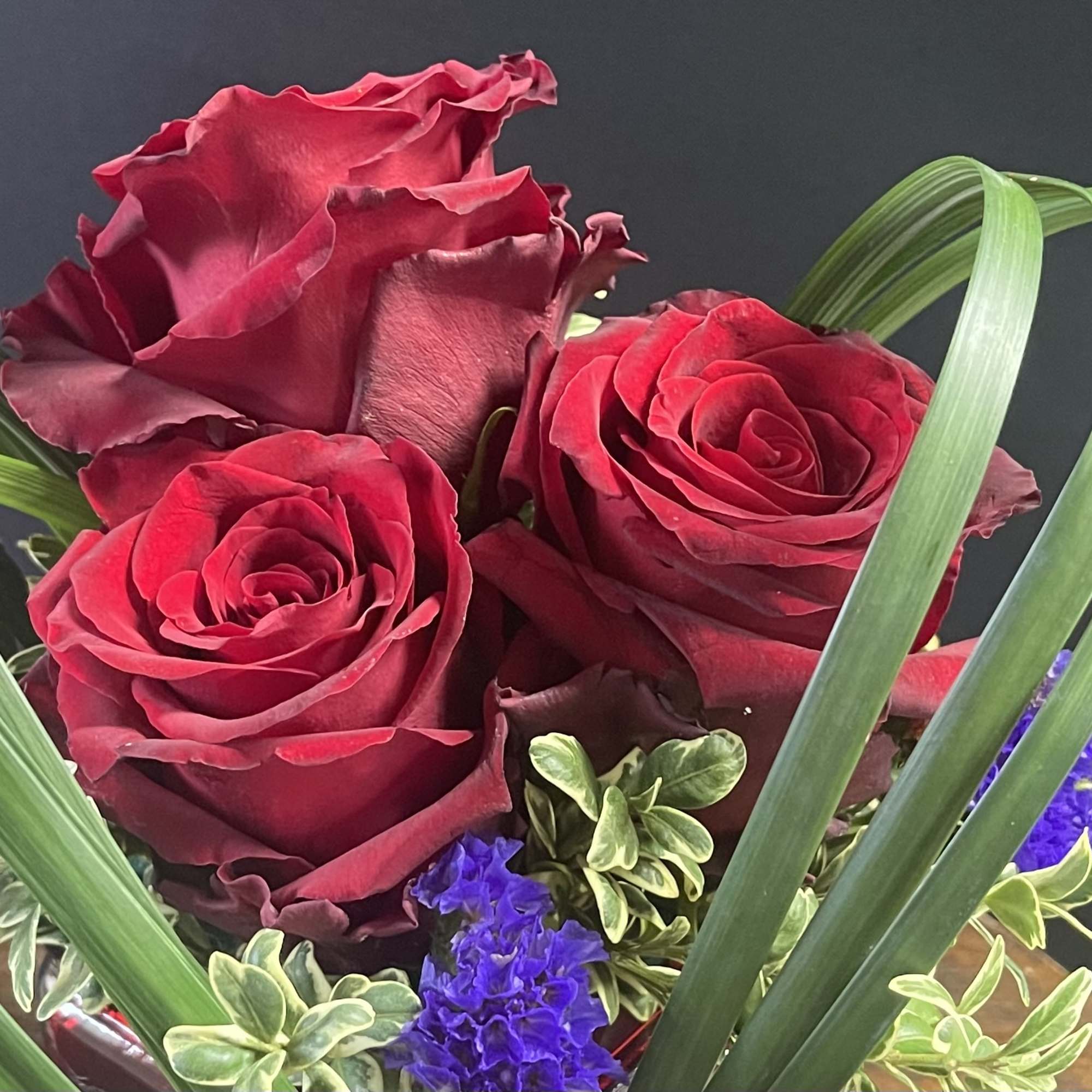 Red roses with purple filler and looping green leaves