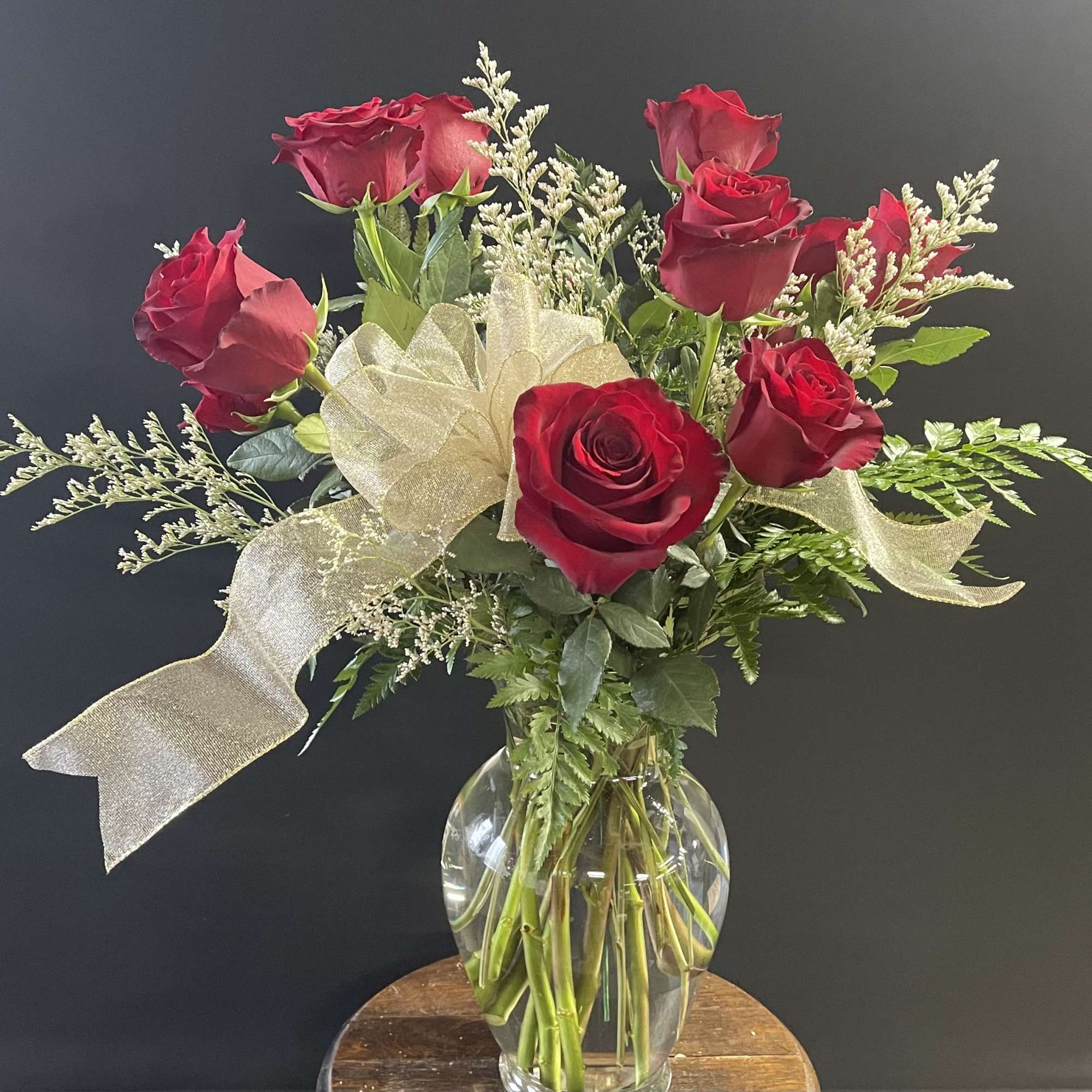 Red roses arranged in a clear glass vase with a gold ribbon