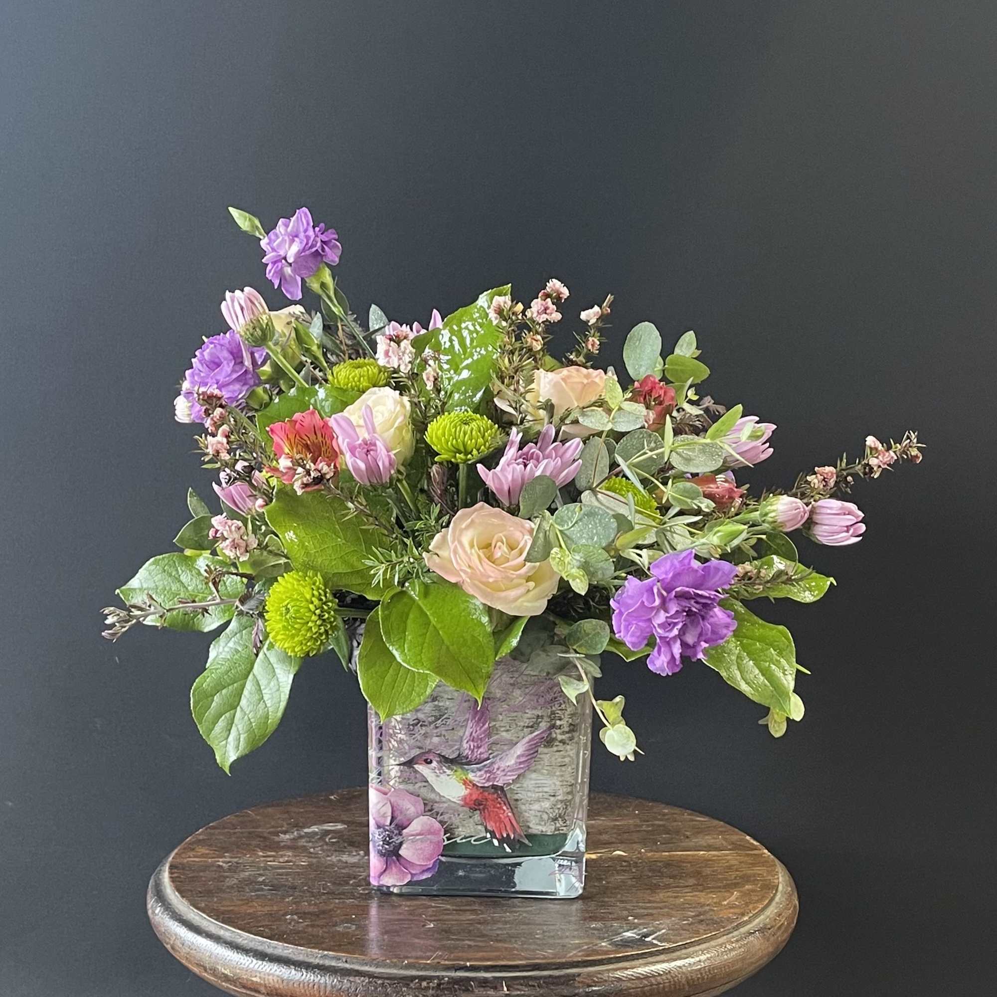 Mixed bouquet in a square glass vase with purple, pink, and green blooms
