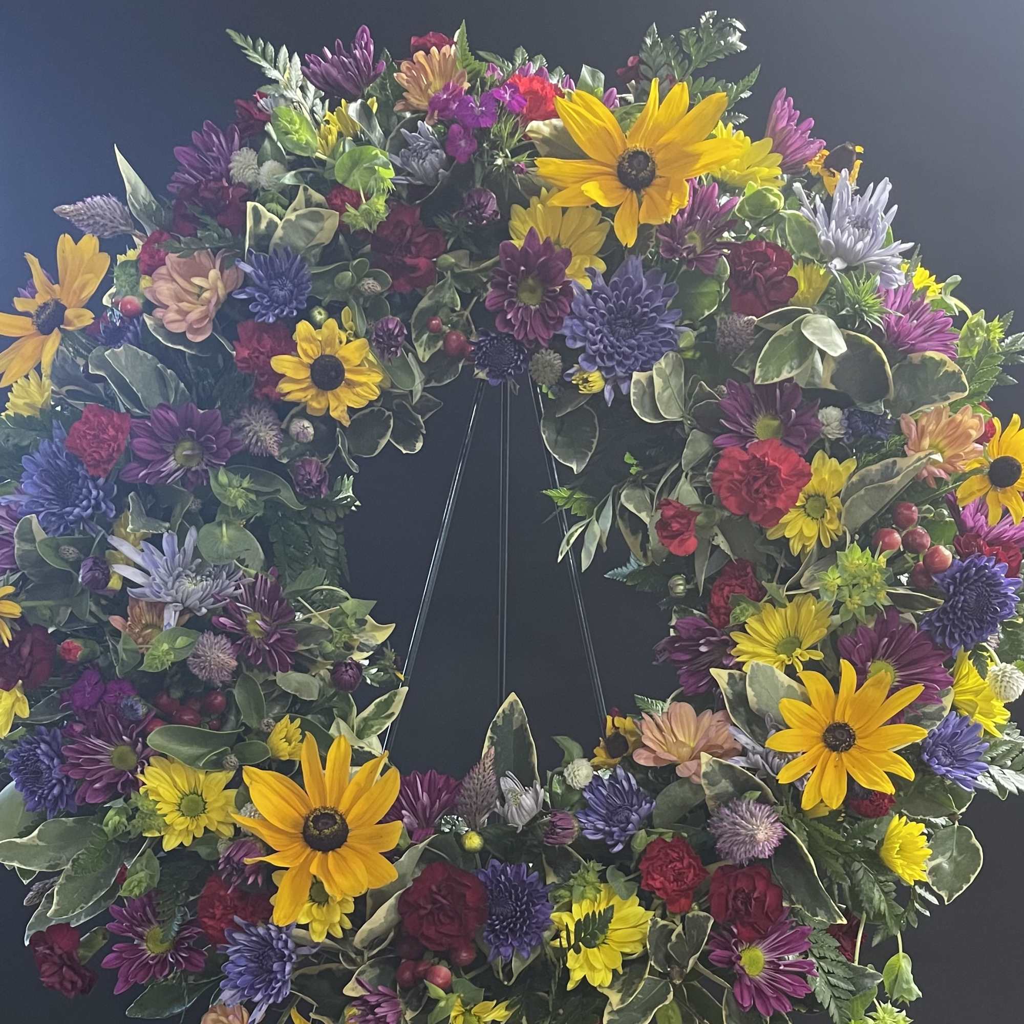 Large floral wreath with yellow daisies and purple blooms on a dark stand