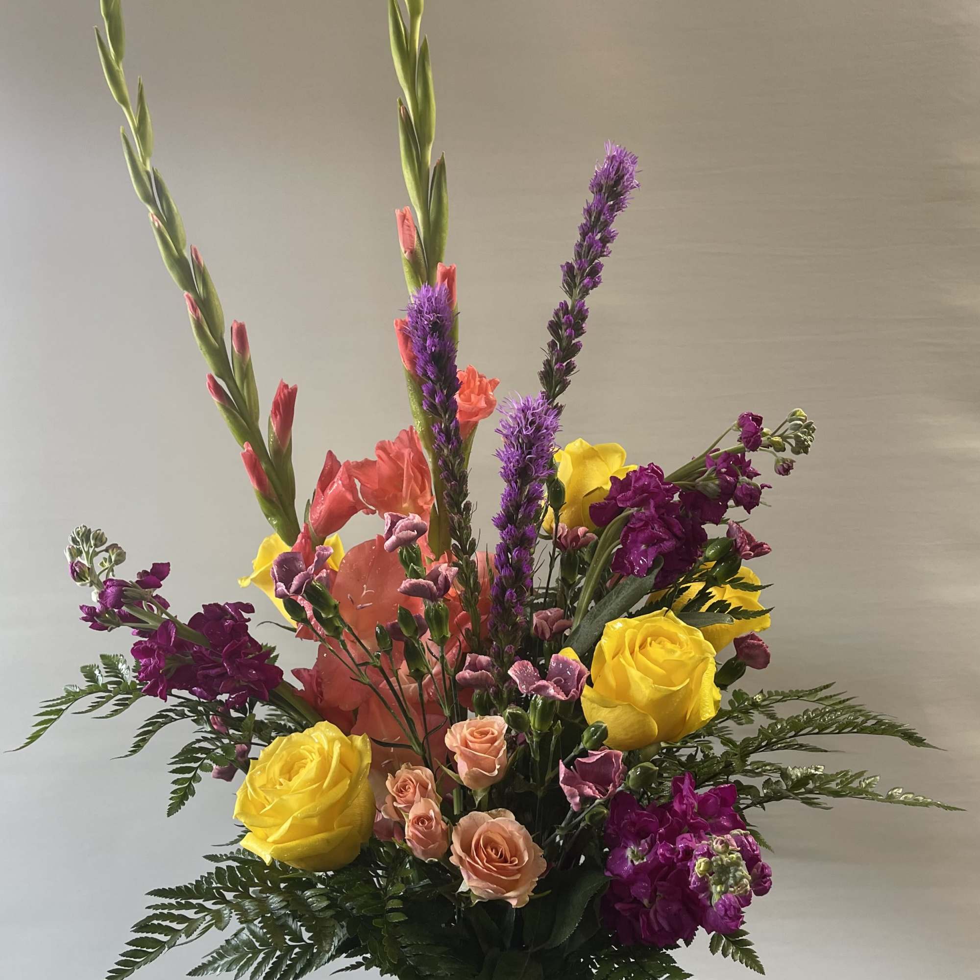Tall mixed bouquet in a clear glass vase with yellow, pink, purple, and coral flowers