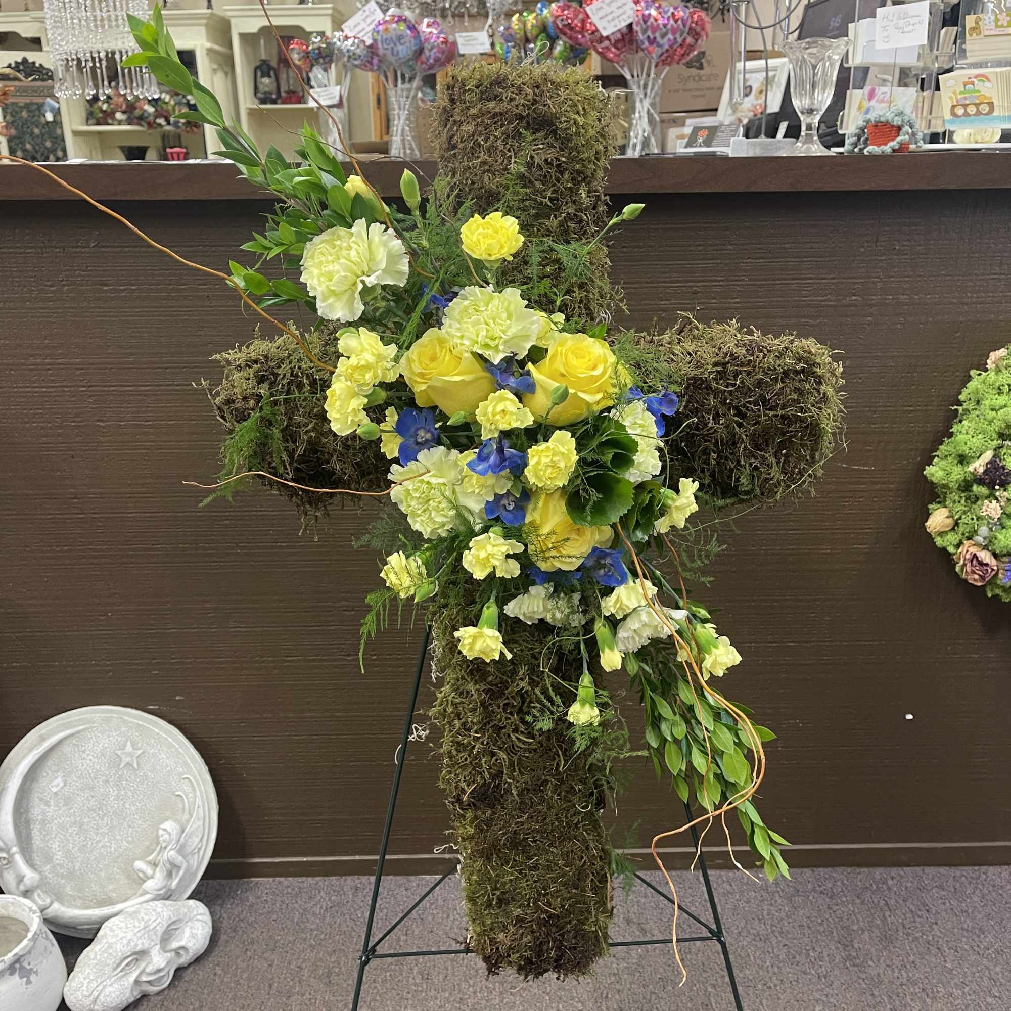 Moss-covered cross arrangement with yellow and white flowers